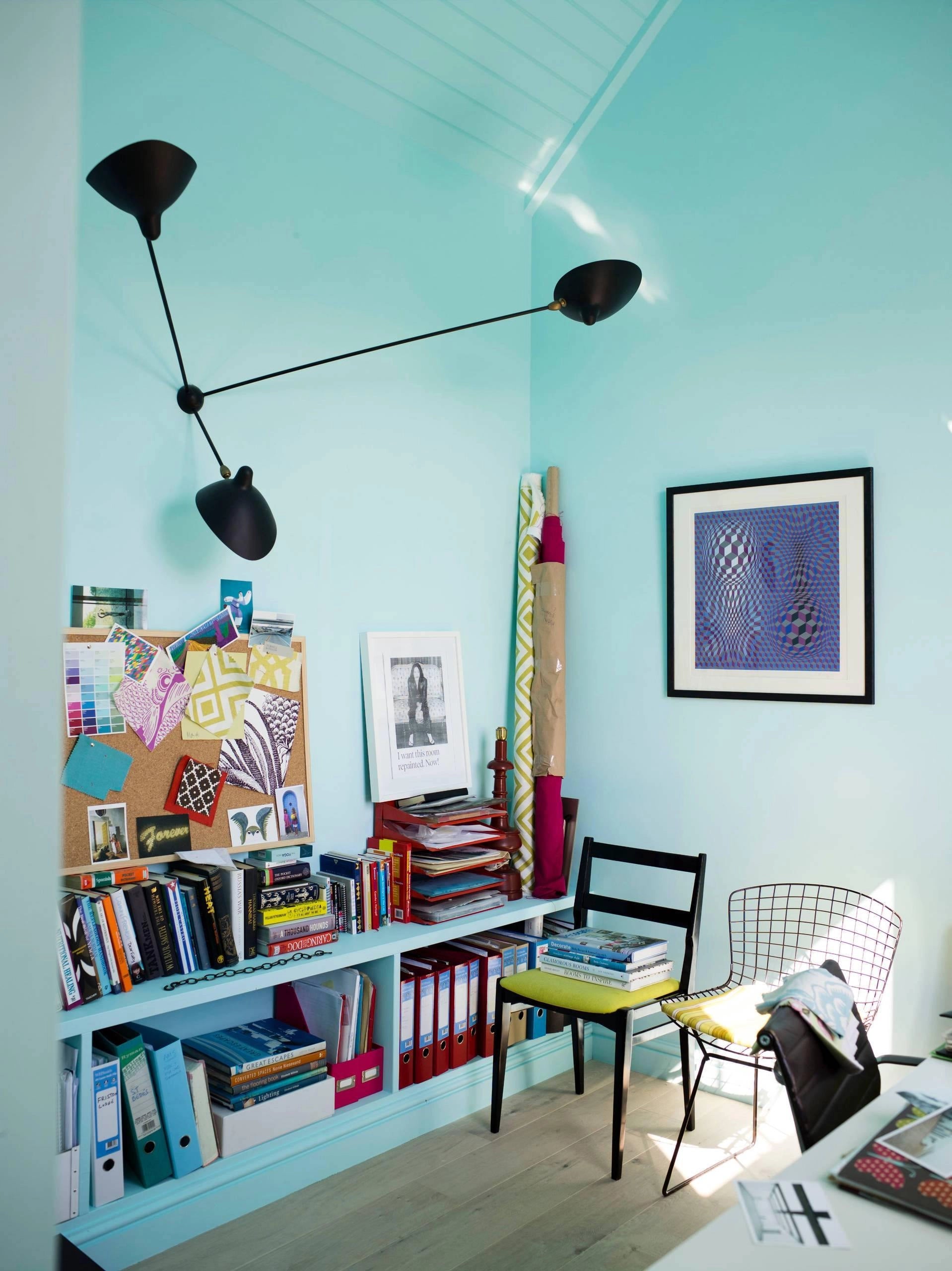 
A modern adjustable black wall lamp installed in a minimalist living room, complemented by furniture such as a picture frame, table, and chair, with a bookcase in the background.