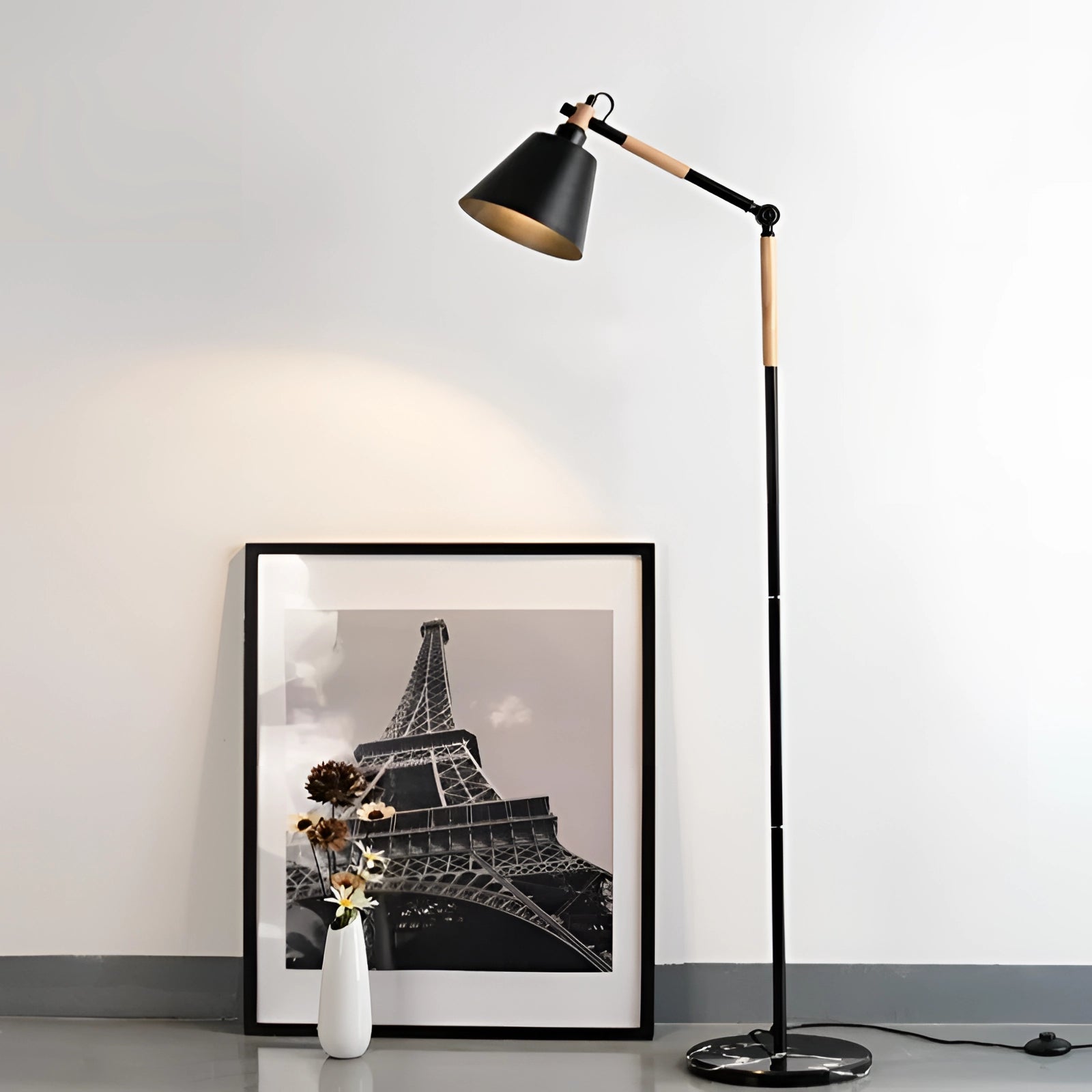 Modern adjustable height floor lamp with a white shade and wooden stand, featuring a movable head, placed in a contemporary room setting with picture frames and art on the wall.