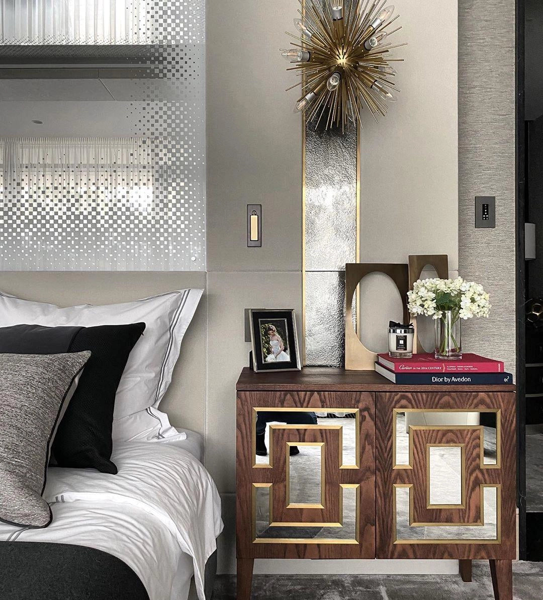 Modern adjustable black LED wall light with weather-resistant finish and motion sensor, mounted on a white wall in a stylish living room interior with wooden furniture, plants, and a picture frame.