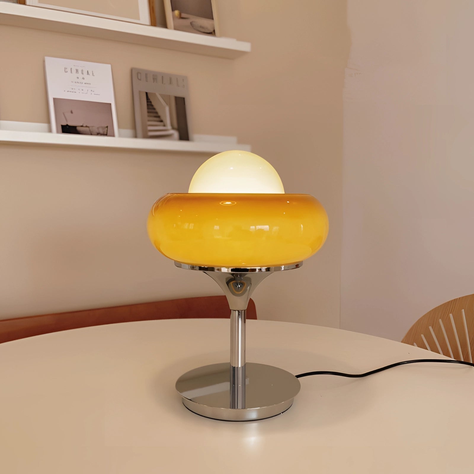 Modern adjustable metal table lamp placed on a wooden table, surrounded by framed art, decorative tableware, and glass items, creating a stylish and ambient home decor setting.