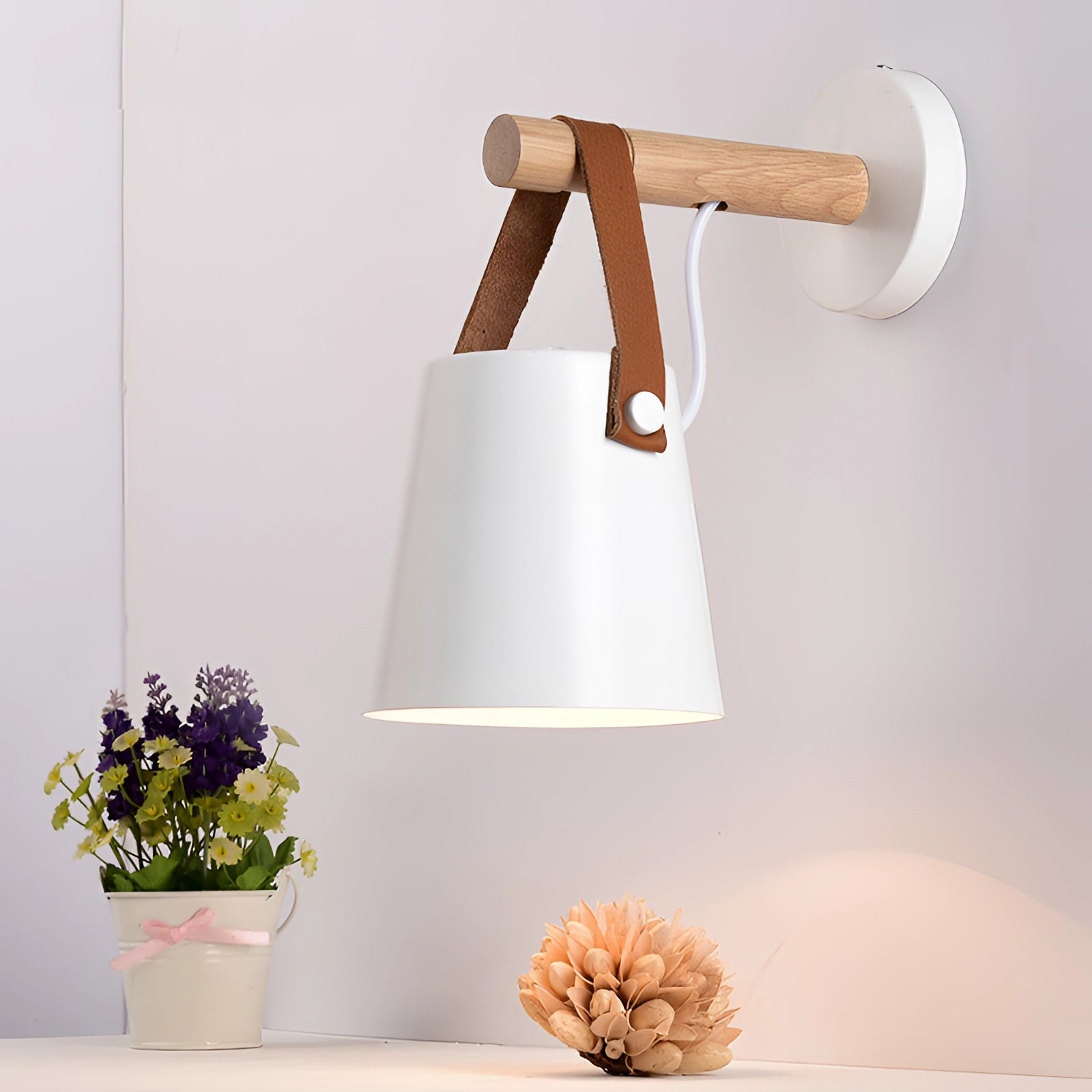 White Scandinavian wooden wall lamp with an adjustable sconce design, mounted on a wall in an interior setting, featuring a combination of wood and metal elements, with a small plant nearby.