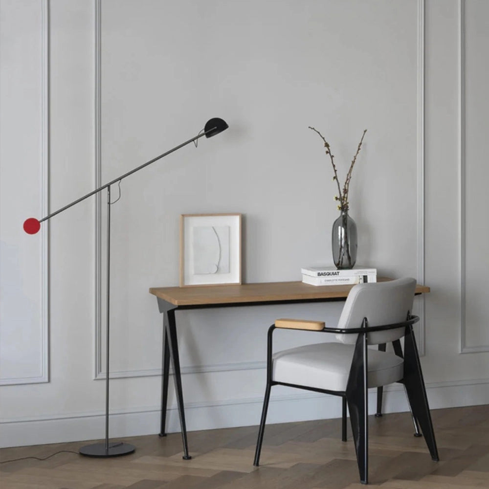 Modern arc floor lamp with a sleek black finish, featuring an adjustable design, positioned next to a wooden table and chair in a contemporary room setting.