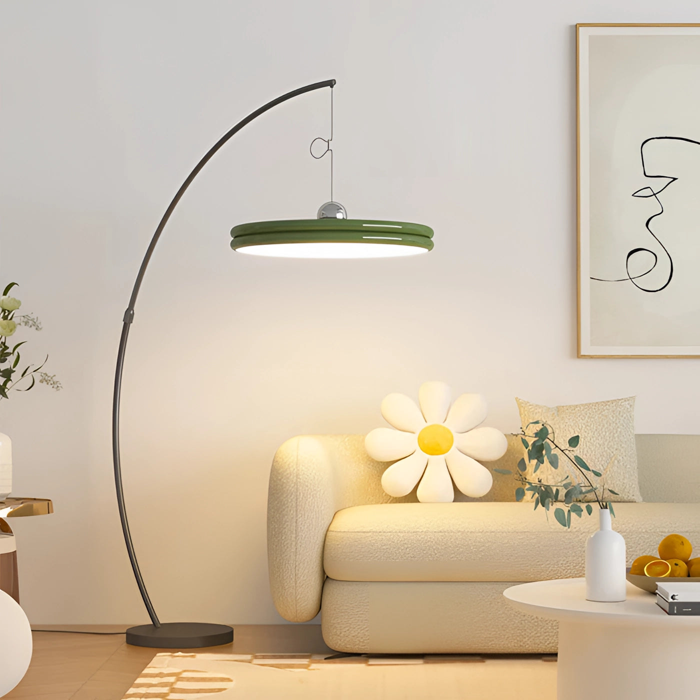 Modern arched floor lamp with a curved metallic finish and a large green shade, positioned in a stylishly furnished interior setting featuring a couch, a potted plant, a table, and decorative wall elements.