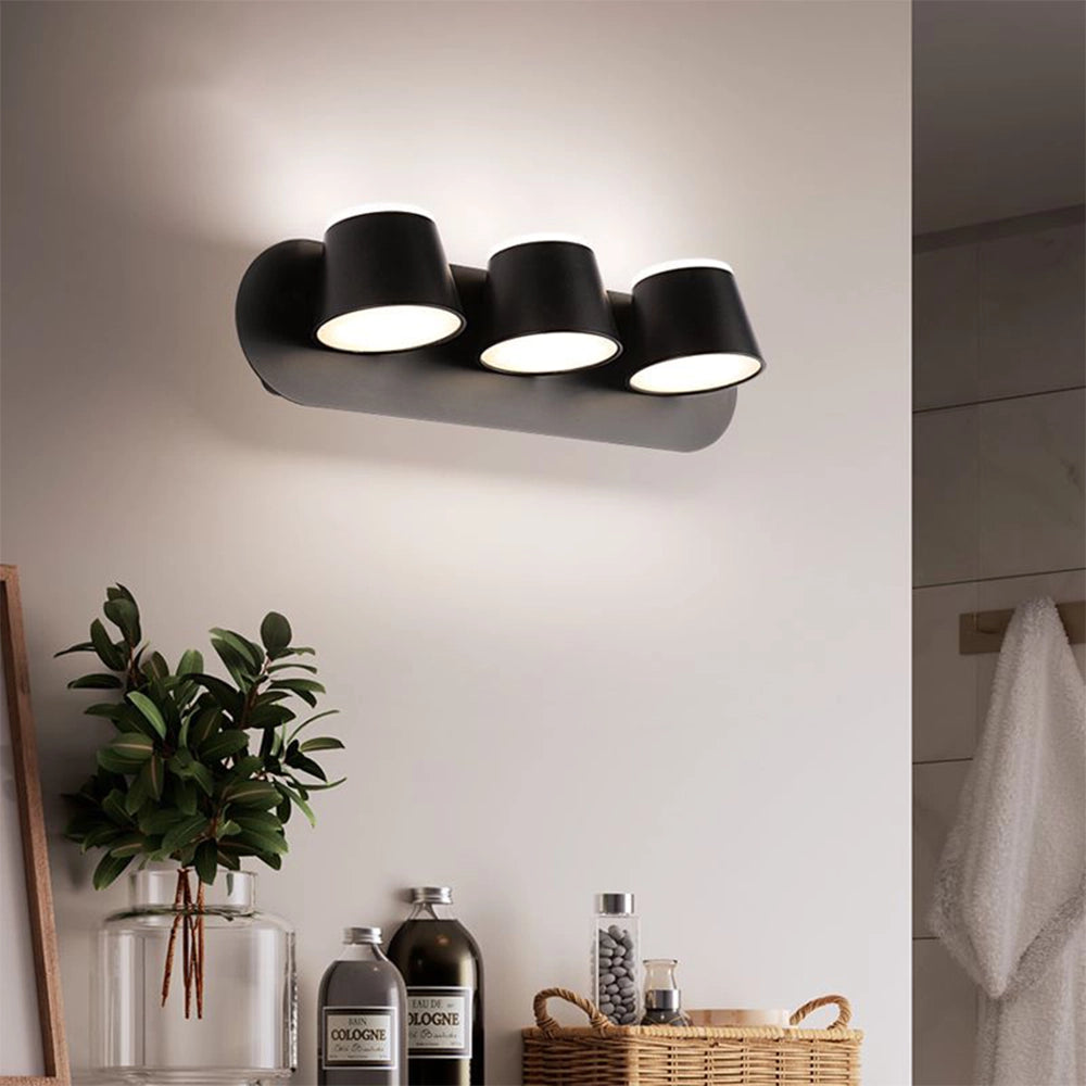 Modern black adjustable 4-light LED track light installed in a room with white walls and wooden shelving, featuring a minimalist interior design with potted plants and decorative bottles.