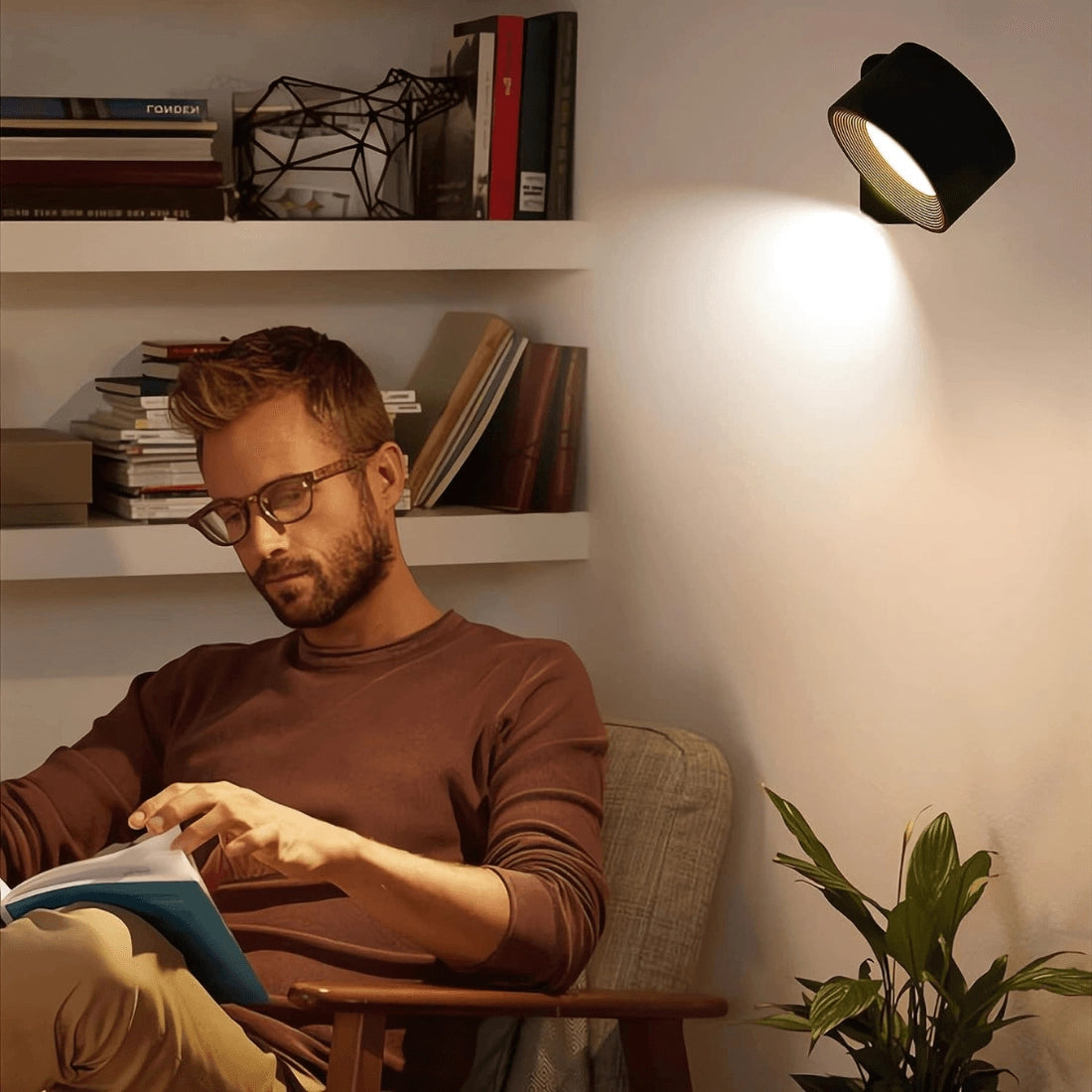Modern black adjustable LED spotlight mounted on a minimalist wall, illuminating a room with shelves, a picture frame, and a small plant nearby.