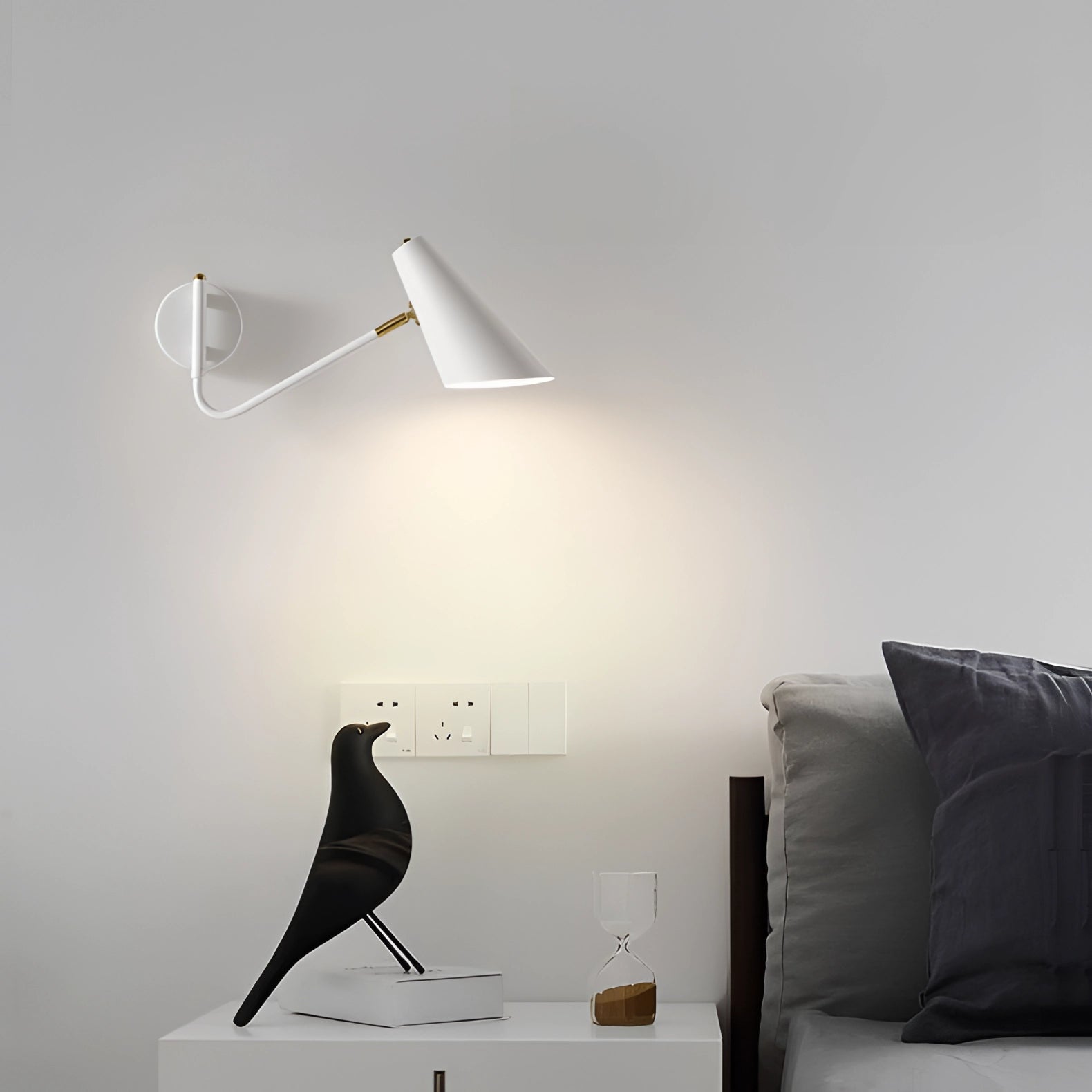 Modern black adjustable wall sconce with a minimalist industrial design, mounted on a grey wall above a wooden surface, providing ambient lighting for a cozy setting.