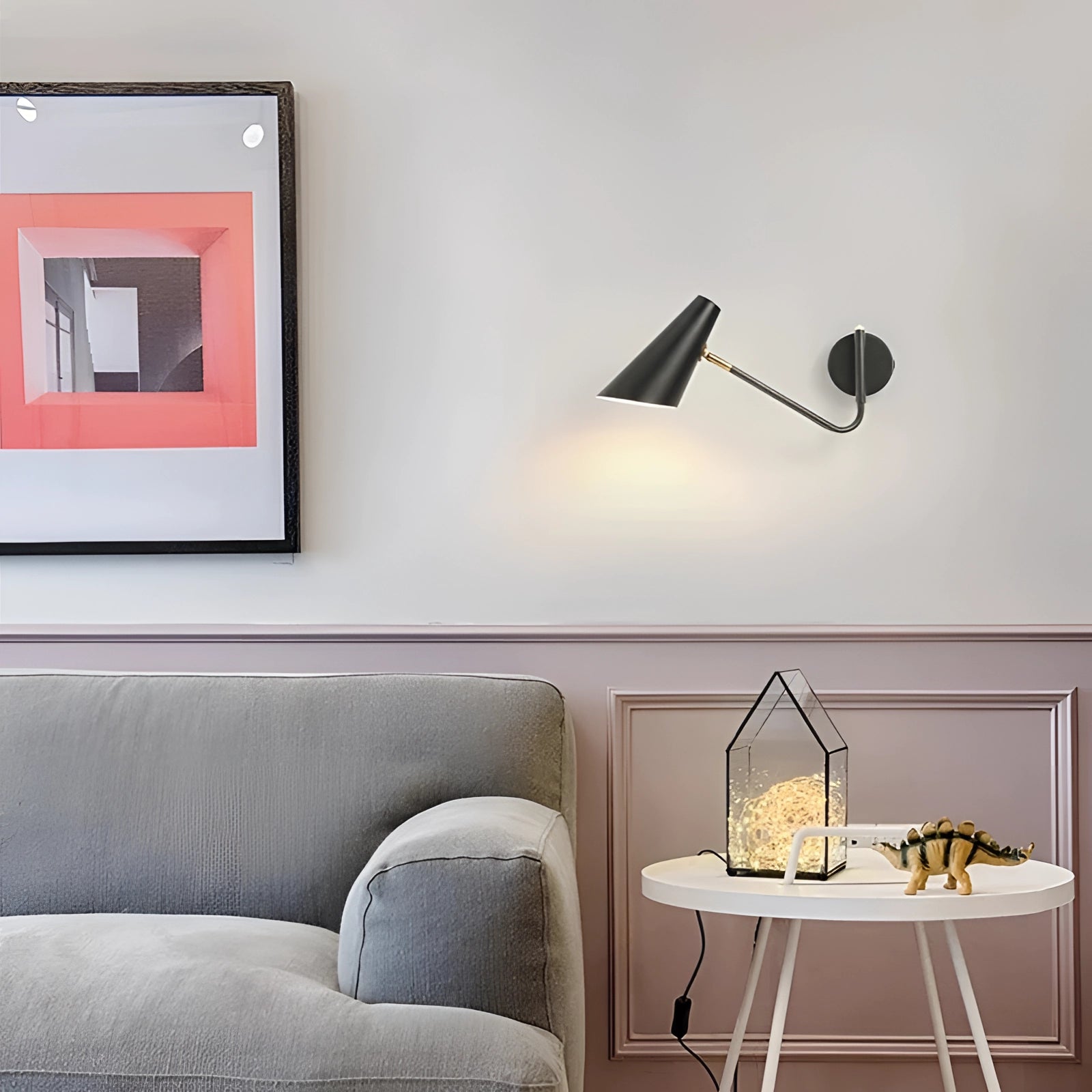 Modern black adjustable wall sconce mounted on a white wall, illuminating a minimalist industrial interior design with nearby furniture including a table and couch.