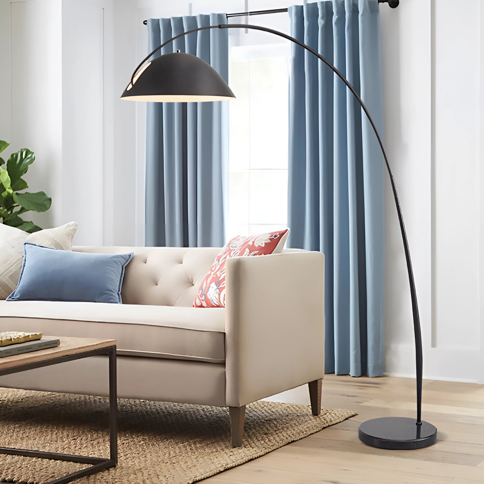 Modern black arched floor lamp with an adjustable dome reading light, standing next to a marble-topped surface in an interior setting with a couch, wooden flooring, and a plant, creating a comfortable and stylish atmosphere.