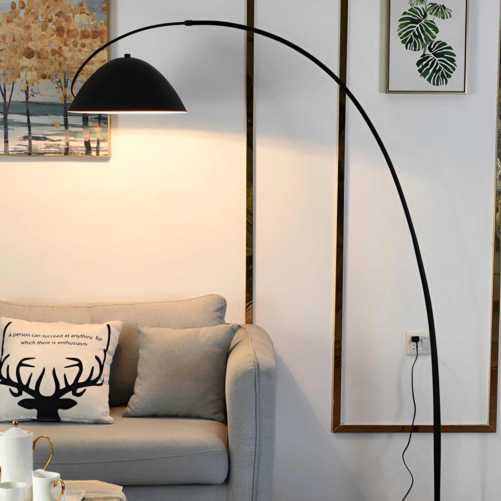 Modern black arched floor lamp with an adjustable dome design, positioned beside a white couch in a stylish interior setting, featuring picture frames and emphasizing comfort and lighting.
