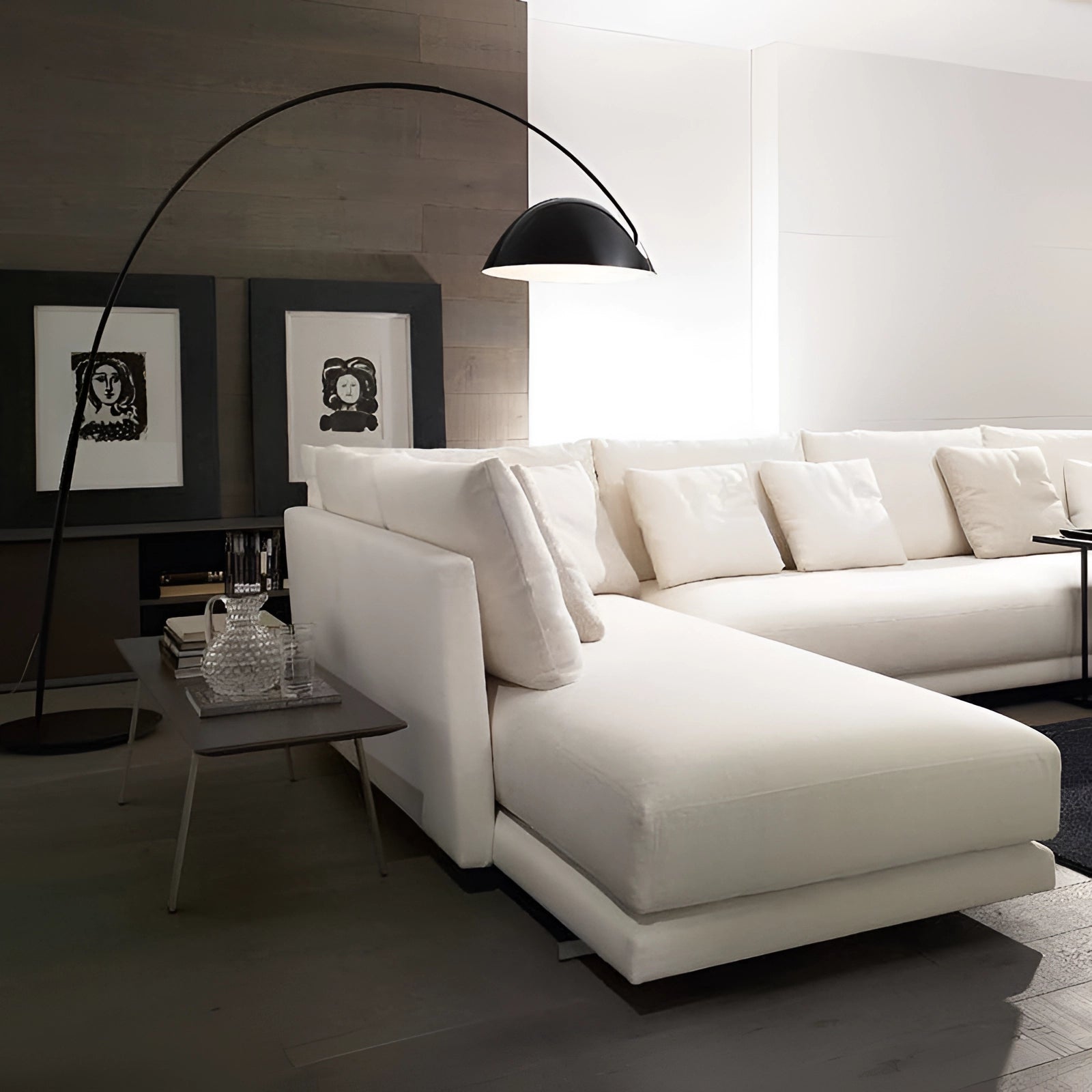 Modern black arched floor lamp with an adjustable dome positioned in a stylish living room setting, featuring a grey studio couch, picture frames, and contemporary interior design elements.