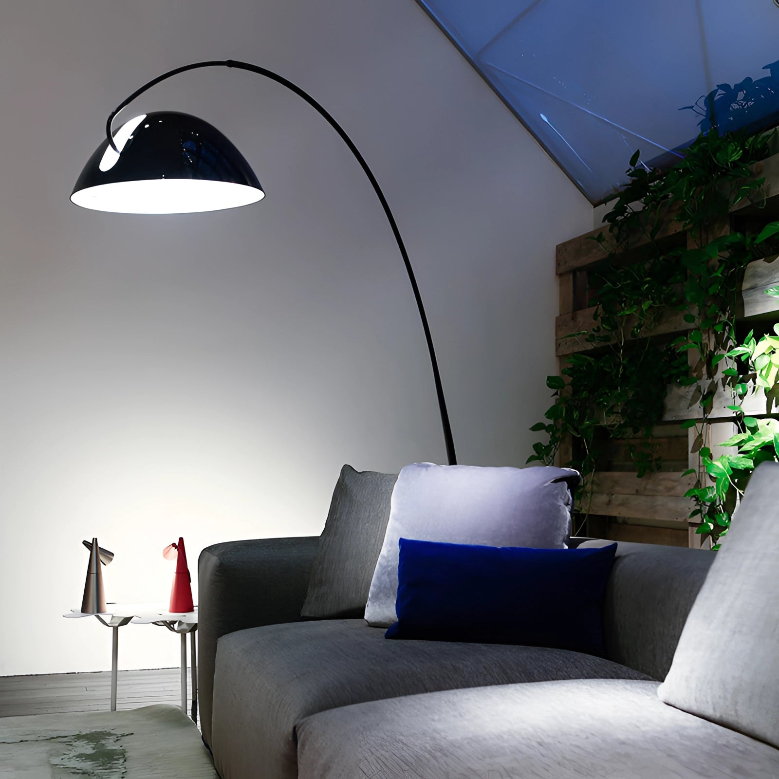 Modern black arched floor lamp with an adjustable dome, situated in a cozy living room with a couch and potted plant, enhancing the interior design and comfort of the space.