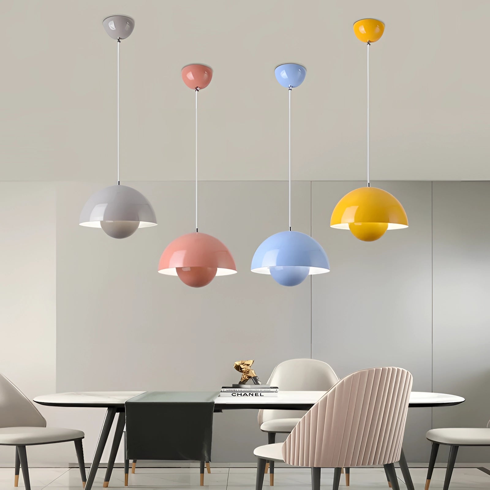 Modern black dome pendant light hanging from the ceiling in a minimalist room setting with a white table, chairs, and artistic wall elements.