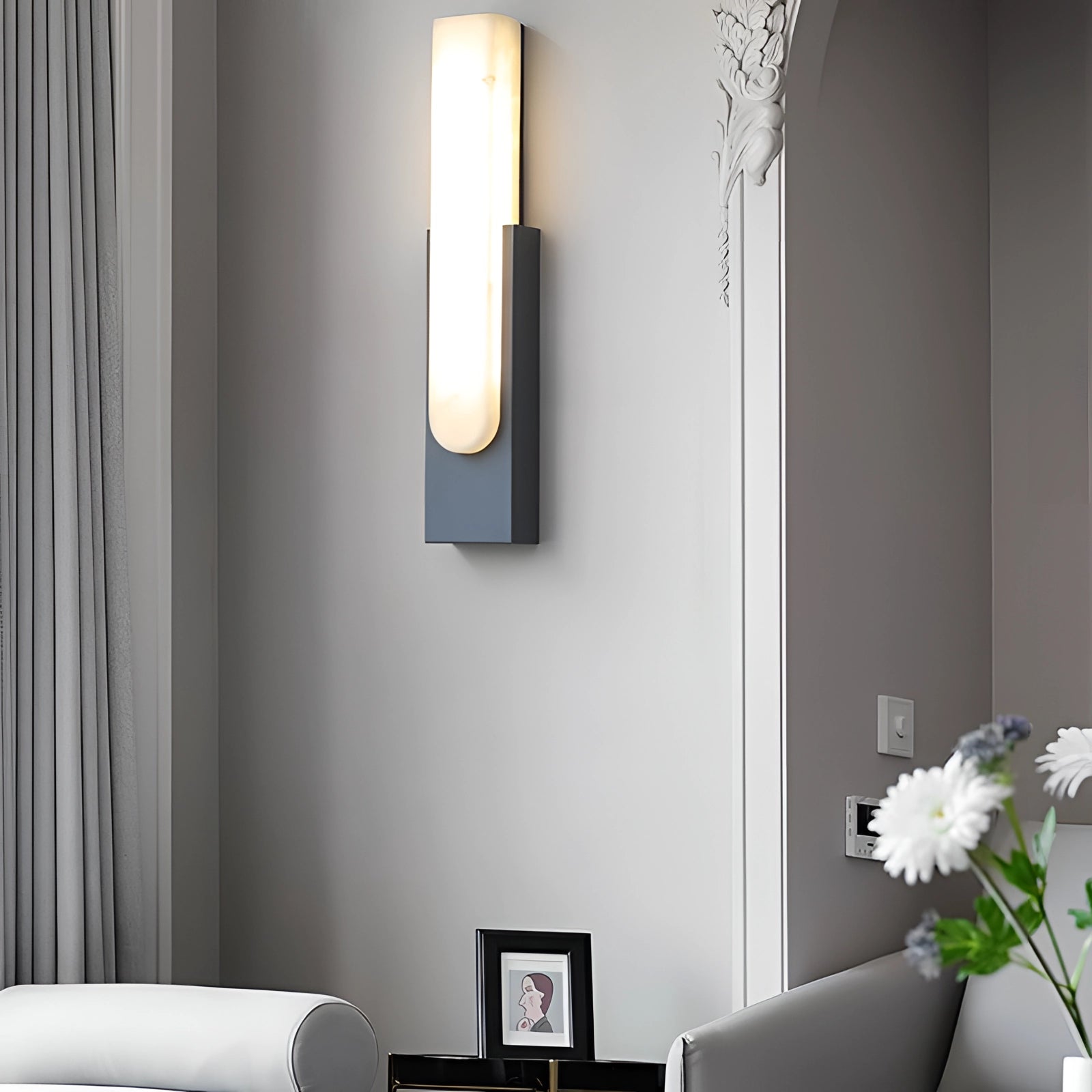 Modern black and gold LED wall sconce with minimalist design mounted on a gray wall, casting illumination in a stylish interior setting.