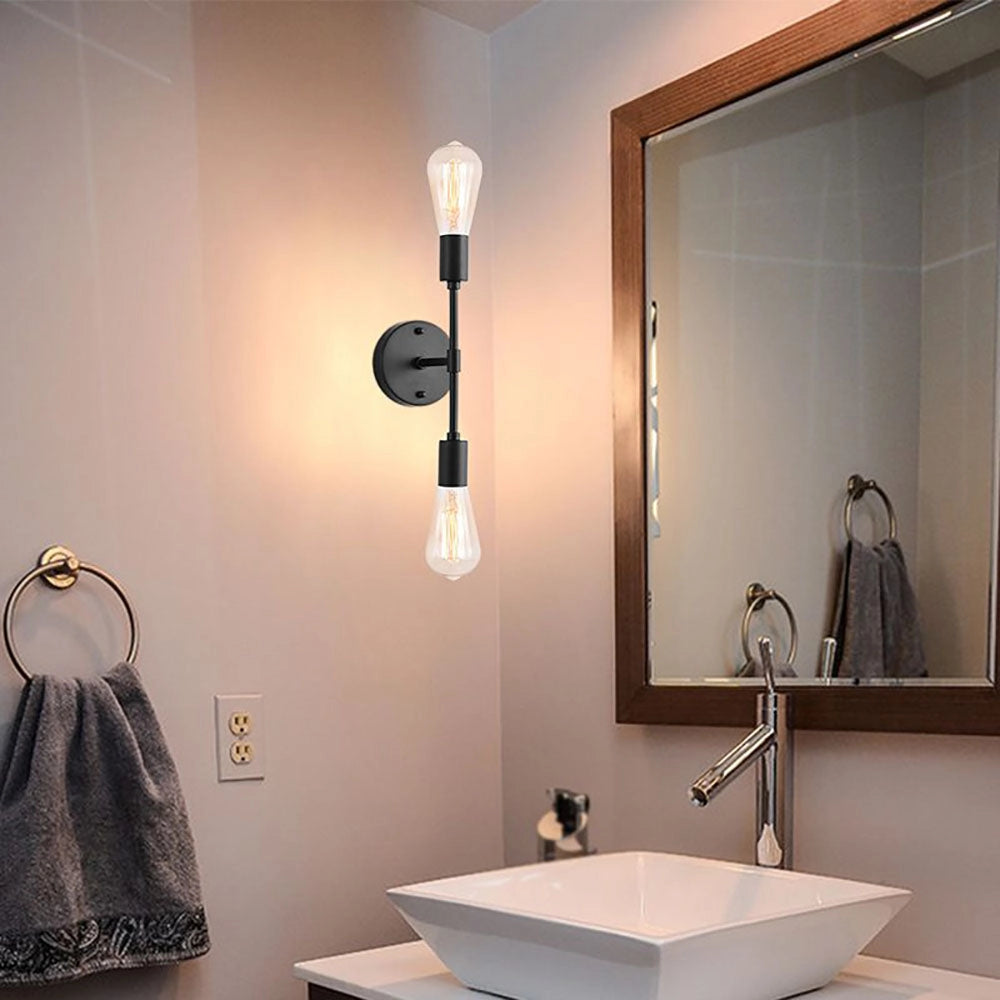 Modern black and gold minimalist wall sconce with an Edison bulb mounted beside a bathroom sink, reflecting softly in a mirror, illuminating the space with warm light.