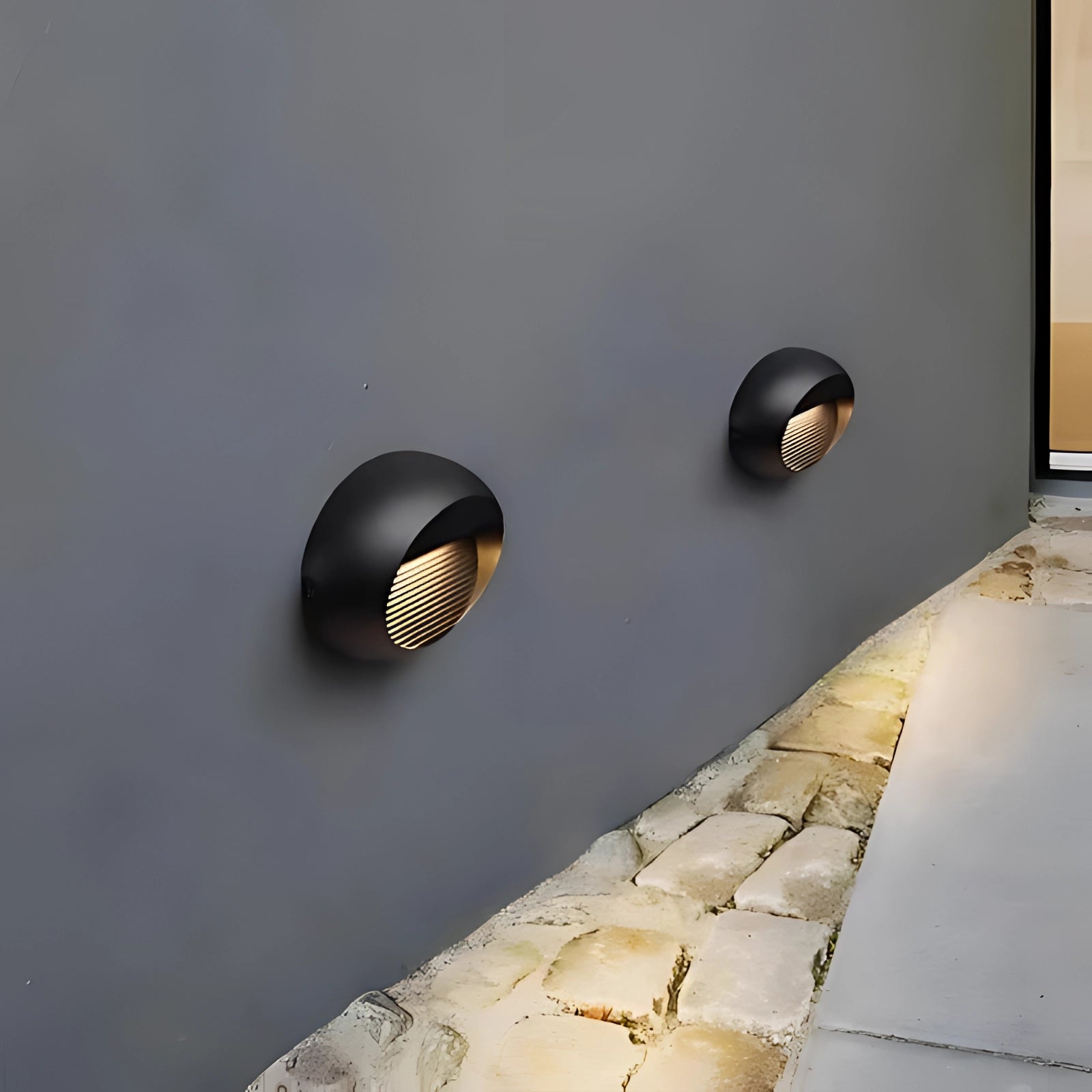 Modern black LED wall sconce mounted on an outdoor wall with a sleek, contemporary design featuring a rectangular fixture. The sconce is shown against a concrete surface and illuminated under a clear sky, highlighting its waterproof capability for outdoor use.