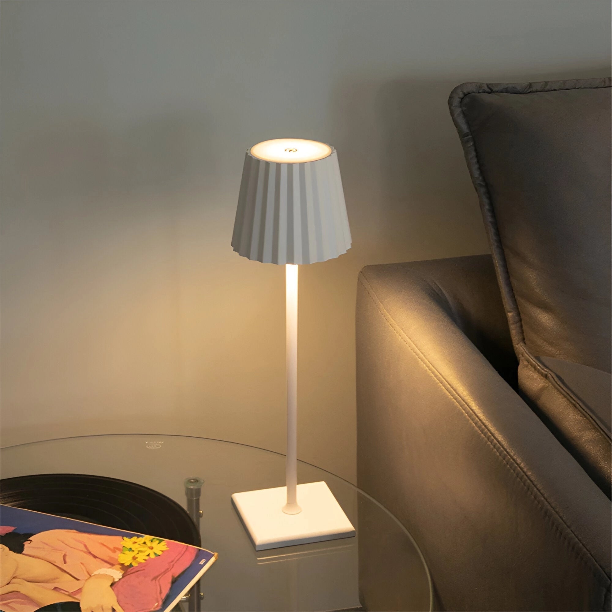 A modern white minimalist LED table lamp with a sleek and elegant design, featuring a simple yet sophisticated shade, placed on a wooden table in a tastefully decorated interior setting.
