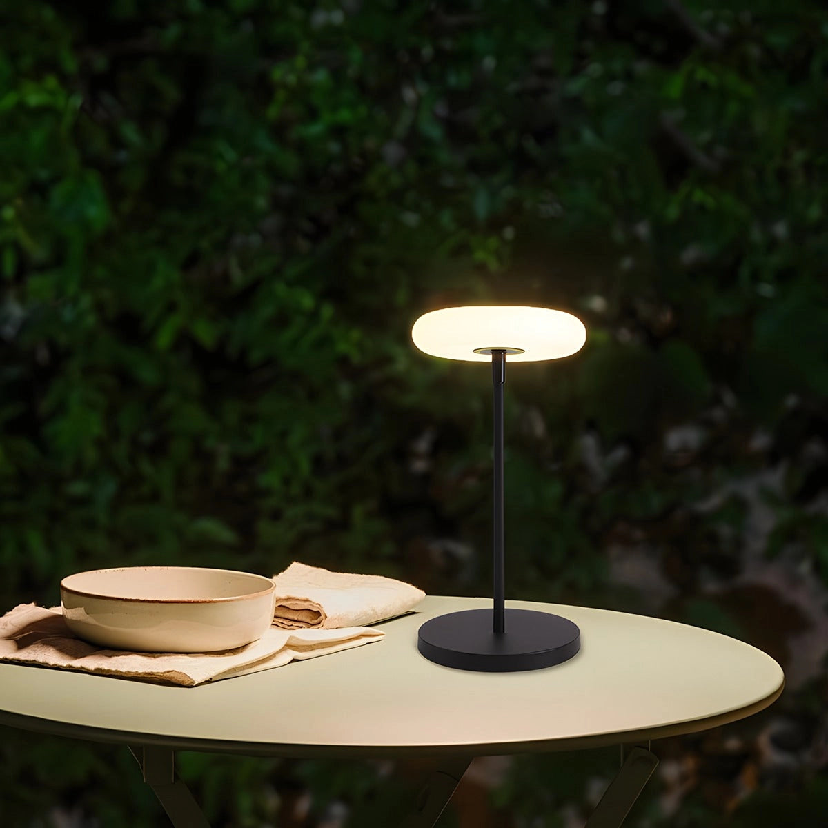 Modern black minimalist LED torchiere floor lamp in a sleek design, standing next to a wooden table with tableware and green plants in the background.