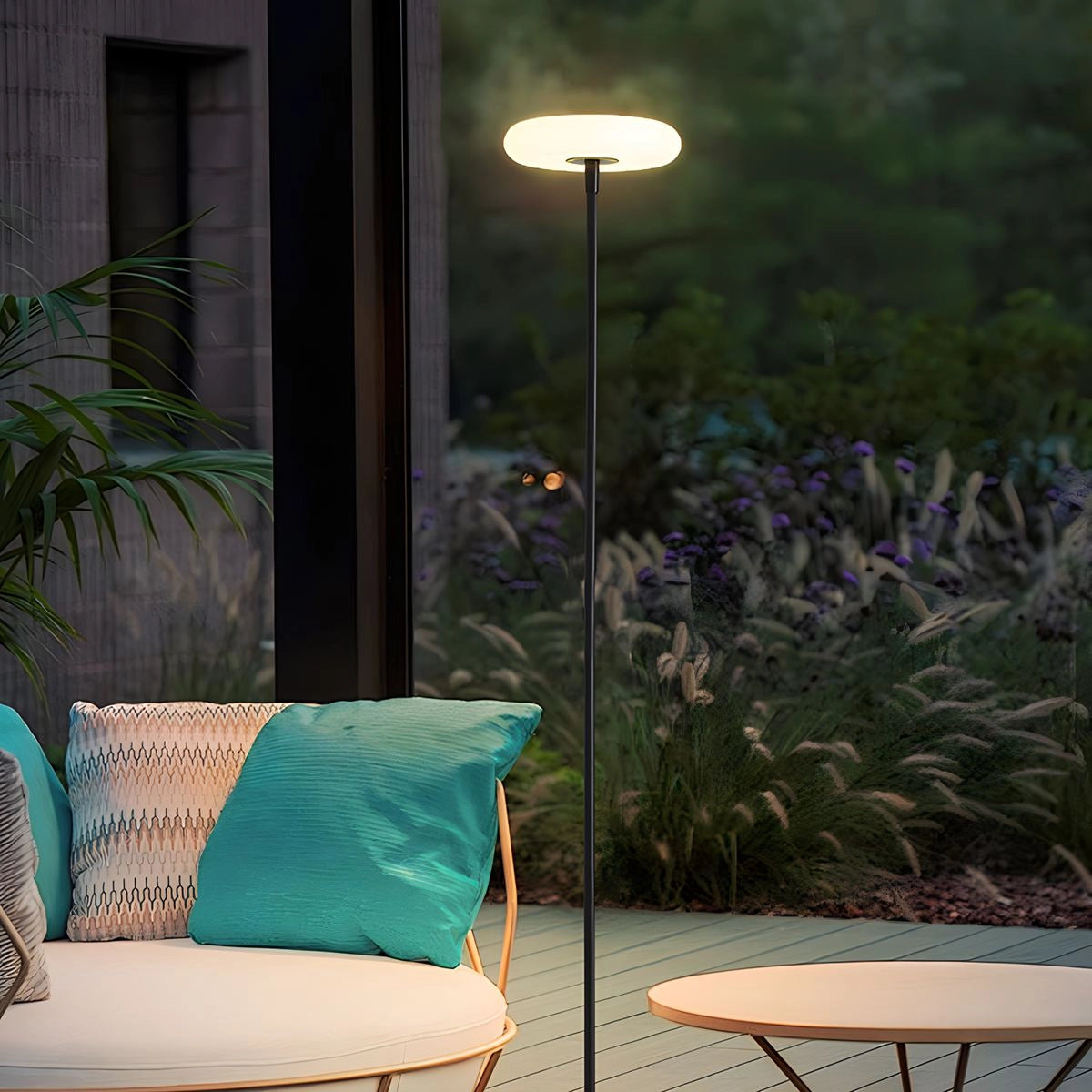 A modern black minimalist LED torchiere floor lamp positioned next to a sleek table with a small plant, set in a contemporary living space with abundant natural light.
