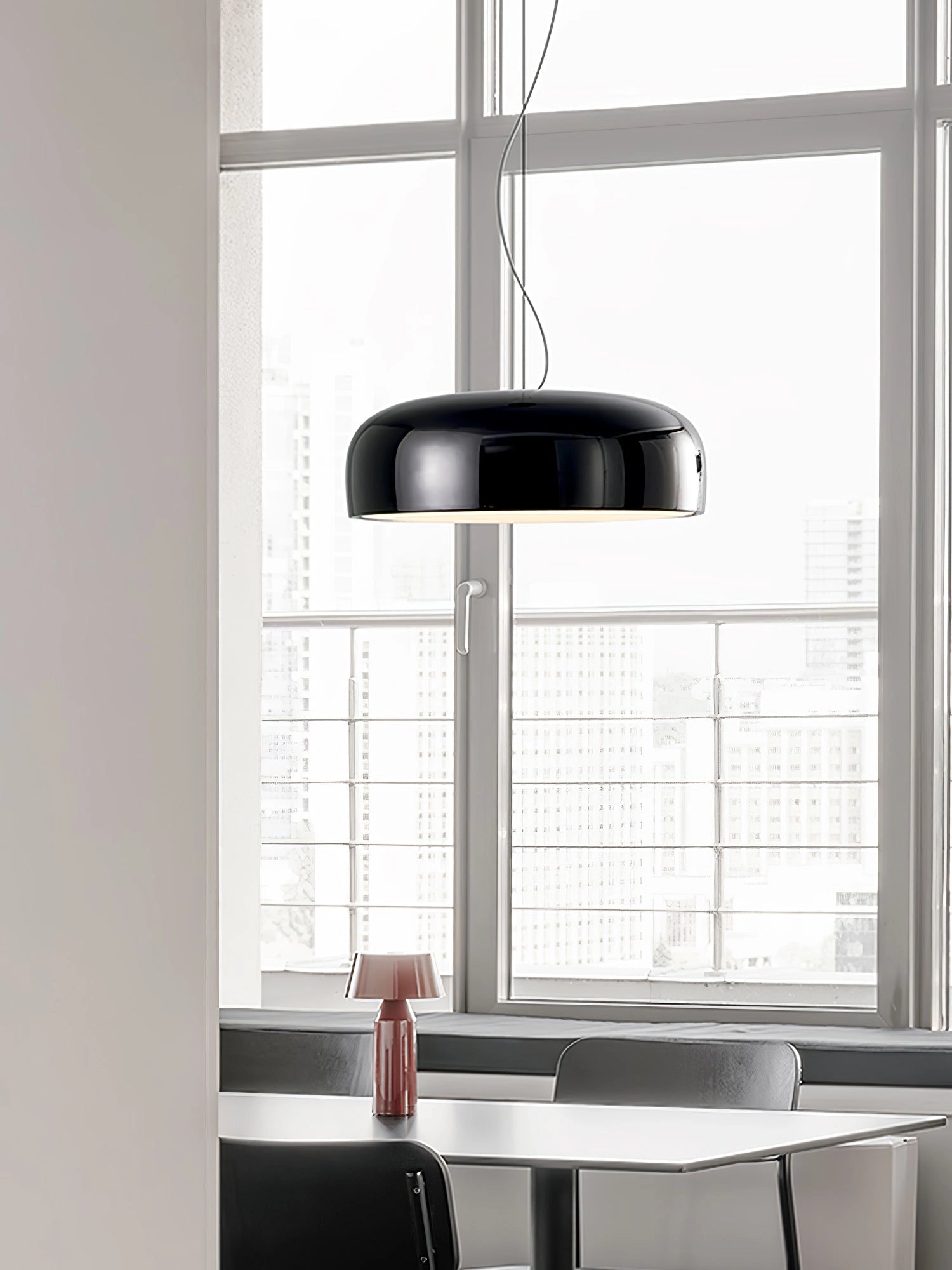 Modern black oval pendant light with a sleek design, hanging over a wooden dining table in a stylishly decorated room with large windows and window blinds.