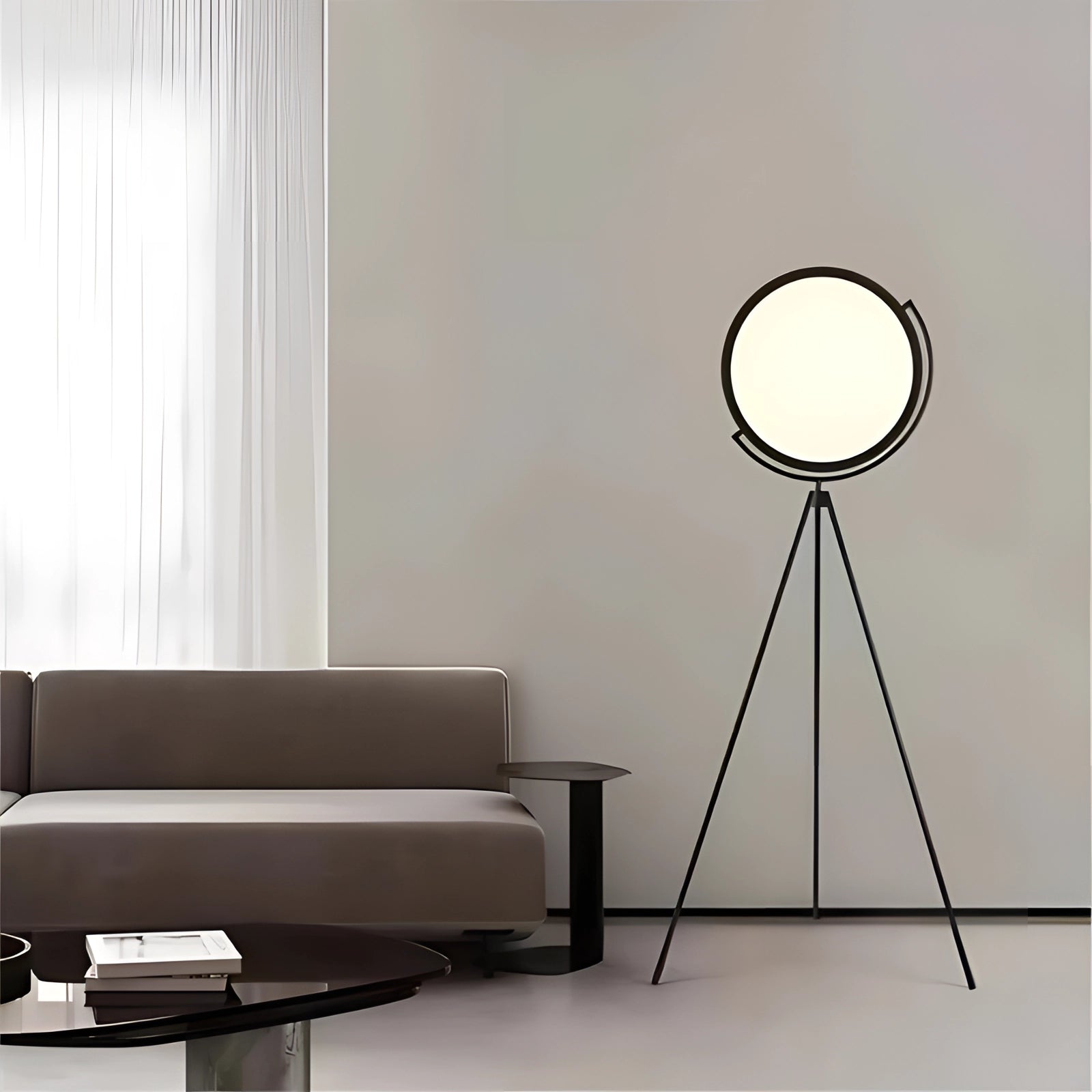 Modern black tripod floor lamp with adjustable features, standing in a stylish interior setting near a grey studio couch, enhancing the minimalist design aesthetic.