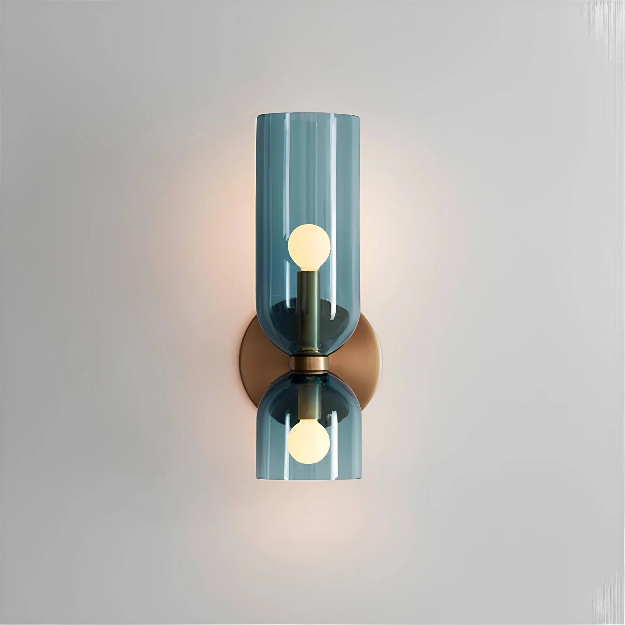 Modern blue glass wall sconce with brass accent, featuring a cylindrical design and luxury lighting elements against a wood backdrop.