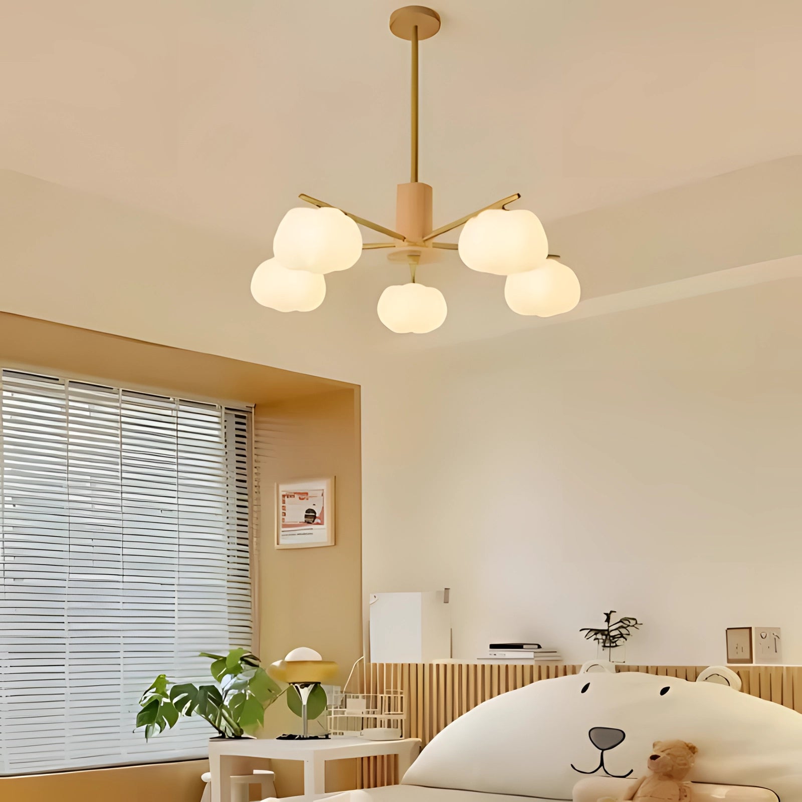 Modern brass chandelier featuring five milk glass globes, hanging from a central fixture with a sleek and sophisticated design. The chandelier is shown in an elegant interior setting with wooden accents and a touch of greenery.
