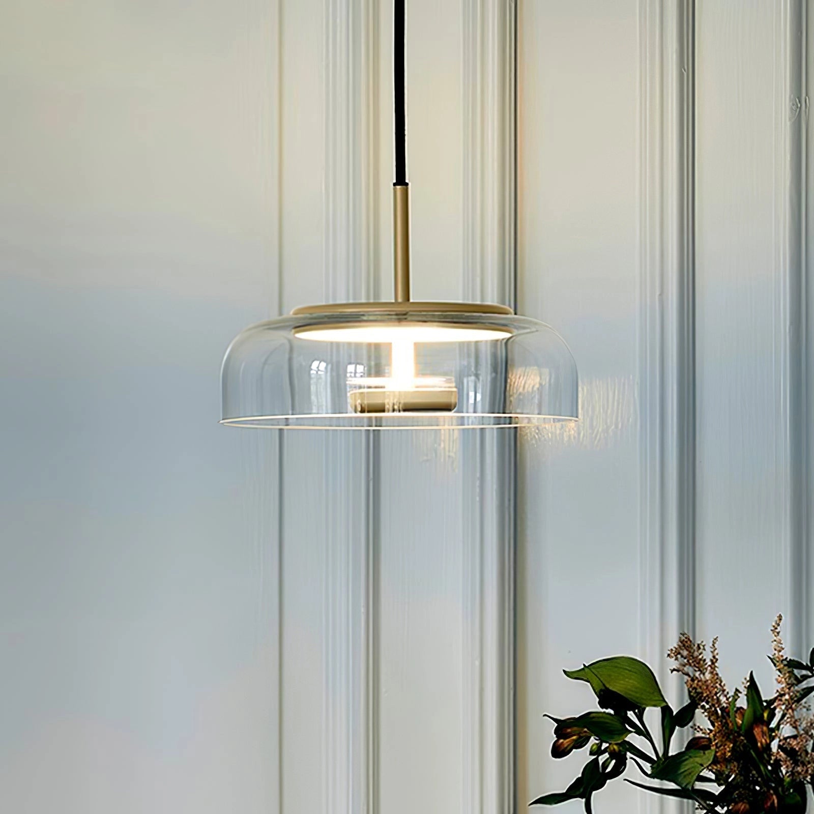 Modern brass and chrome LED pendant lights with minimalist design hanging from the ceiling, illuminating a stylish interior space with wood accents and contemporary decor elements including plants.