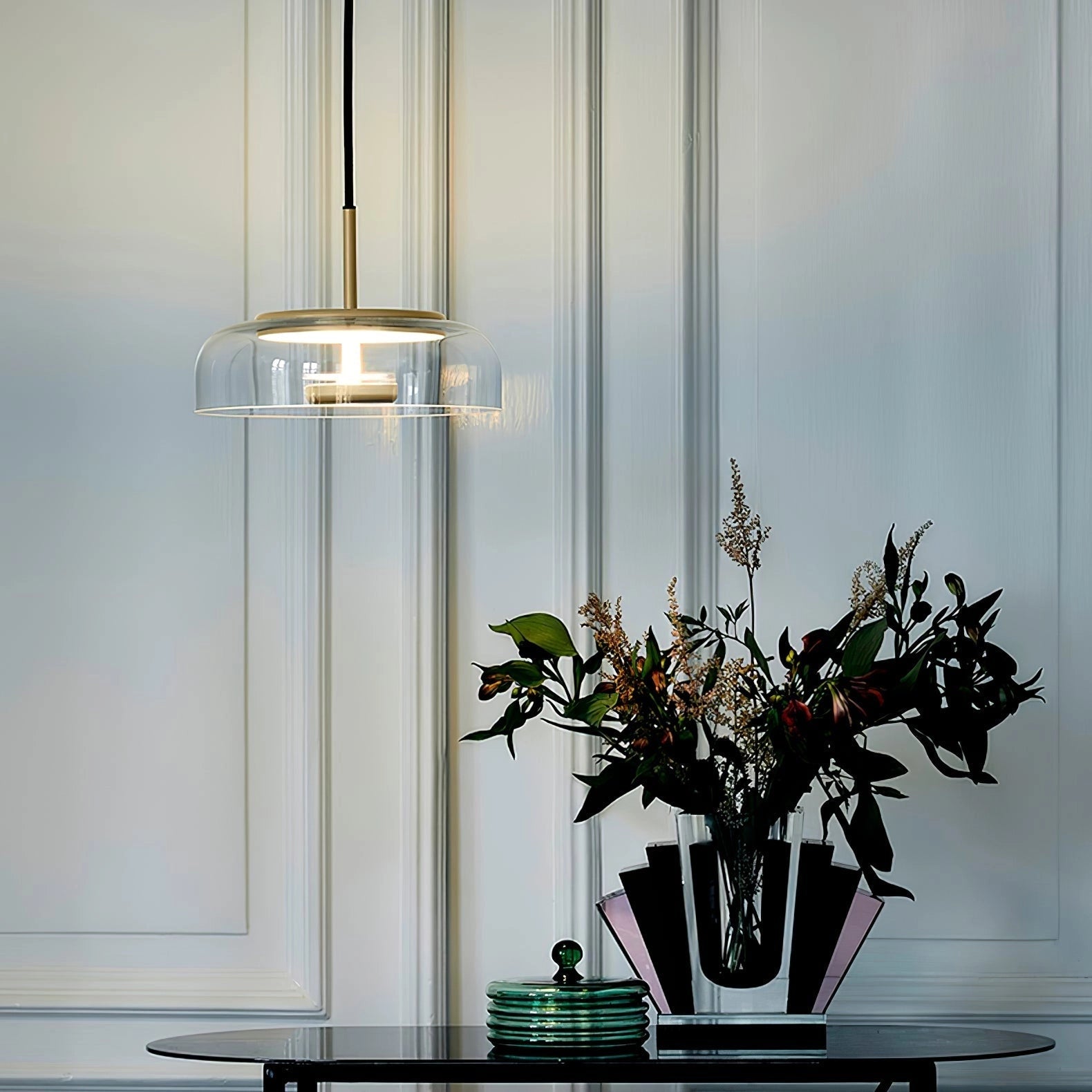 Modern brass and chrome LED pendant lights illuminating a minimalist luxury interior with a wooden table, flower vase, potted plant, twig decor, and picture frames.
