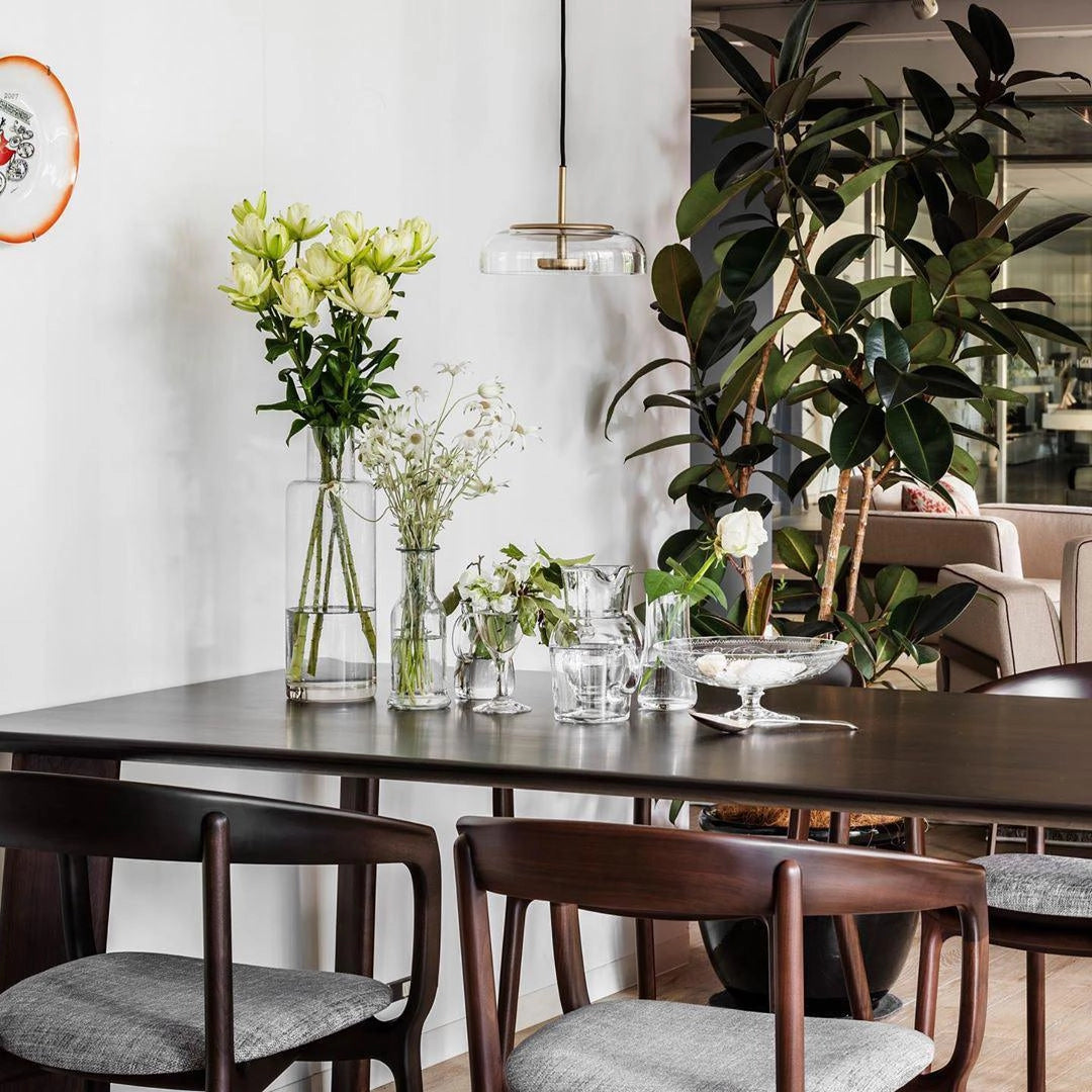 A modern brass and chrome LED pendant light hanging above a stylish table with a decorative vase, flowers, and a houseplant, showcasing a luxury minimalist interior design.