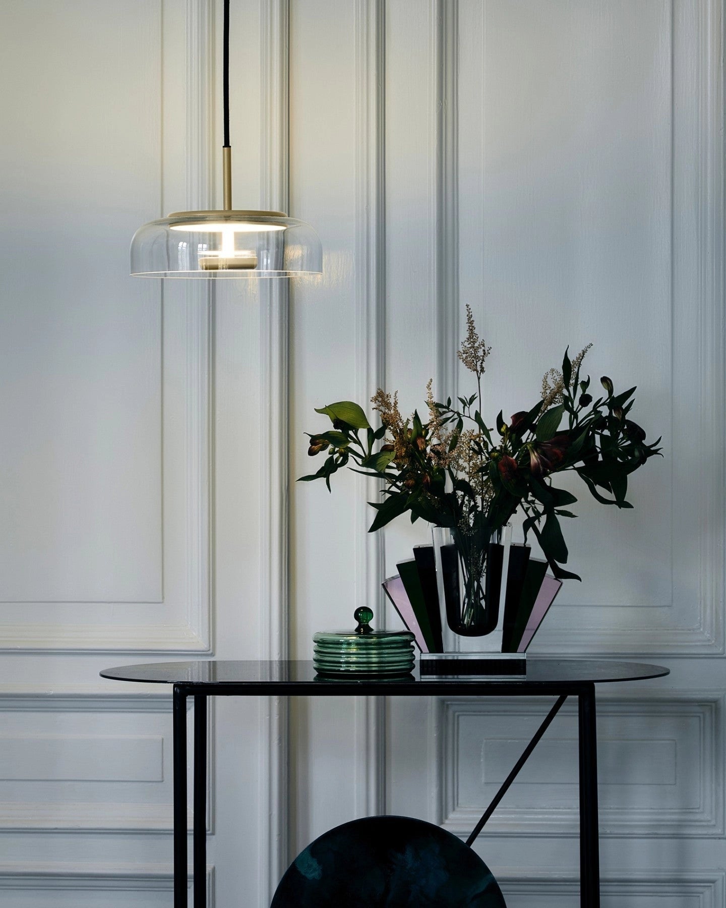 Modern brass and chrome LED pendant lights hanging above a table with a vase, flowers, and houseplants placed nearby, enhancing the minimalist interior decor.