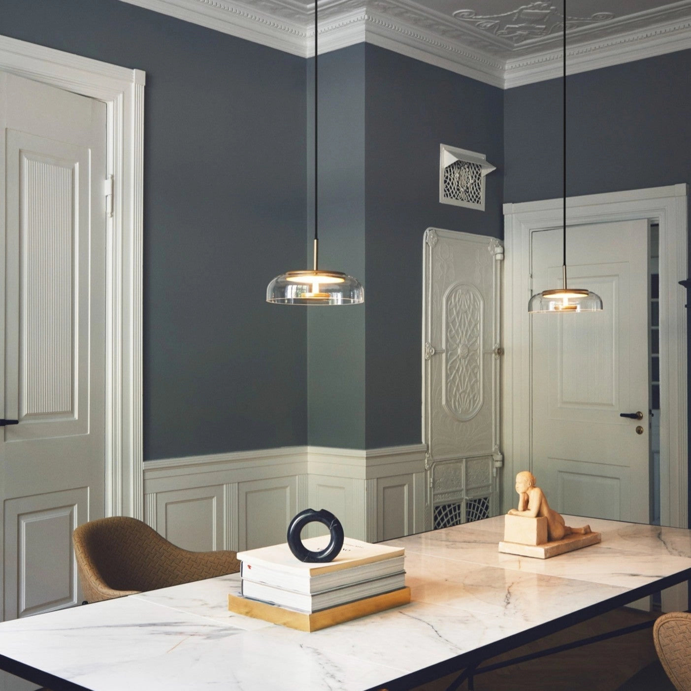 Modern brass and chrome LED pendant lights hanging from the ceiling, illuminating a minimalist living room interior with wooden flooring and contemporary furniture.