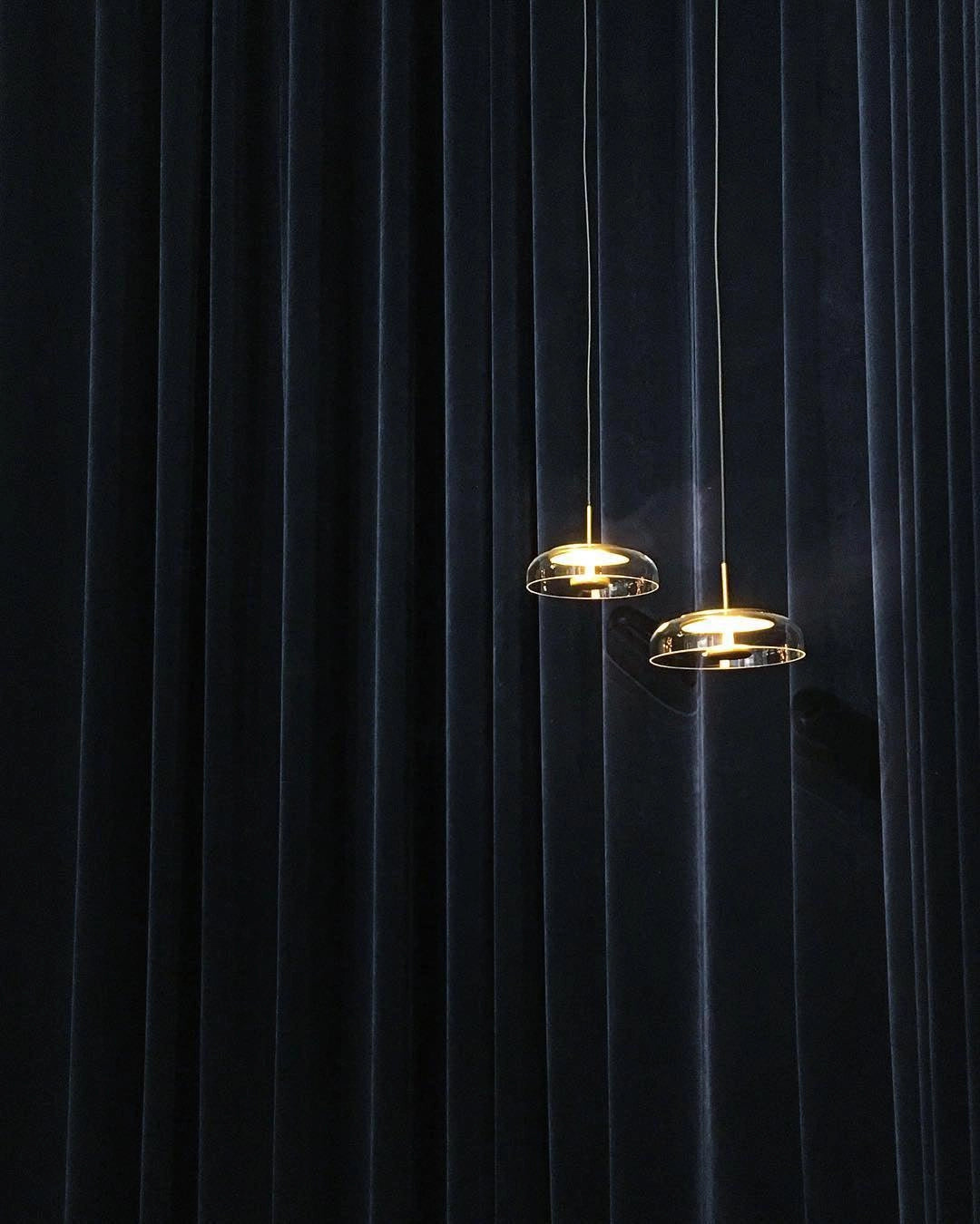 Modern brass and chrome LED pendant lights with a luxury minimalist design hanging from the ceiling, emitting a soft glow against a dark background.