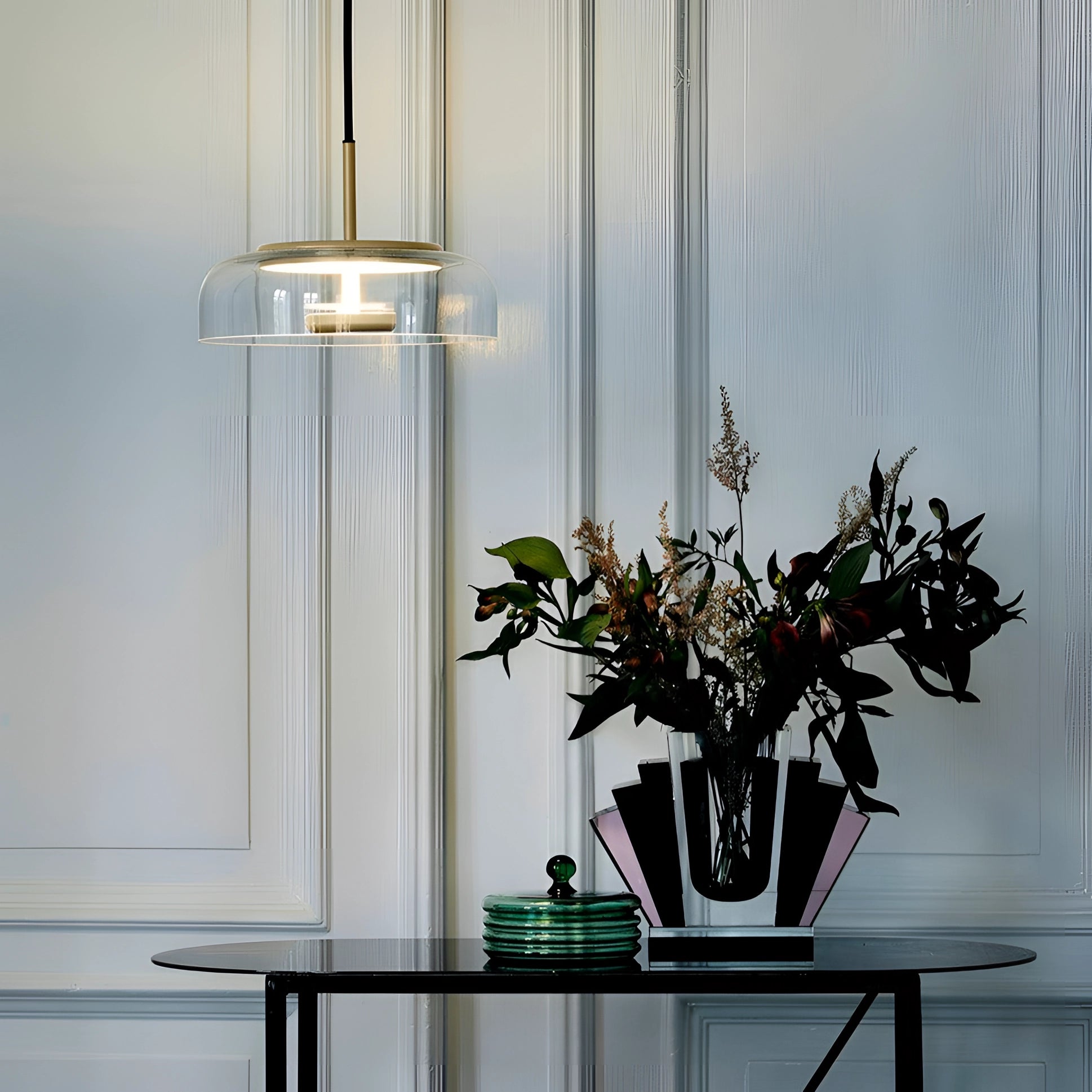 Modern brass and chrome LED pendant lights hanging above a minimalist interior setting featuring a white table with a flowerpot and houseplant near a window with grey curtains.