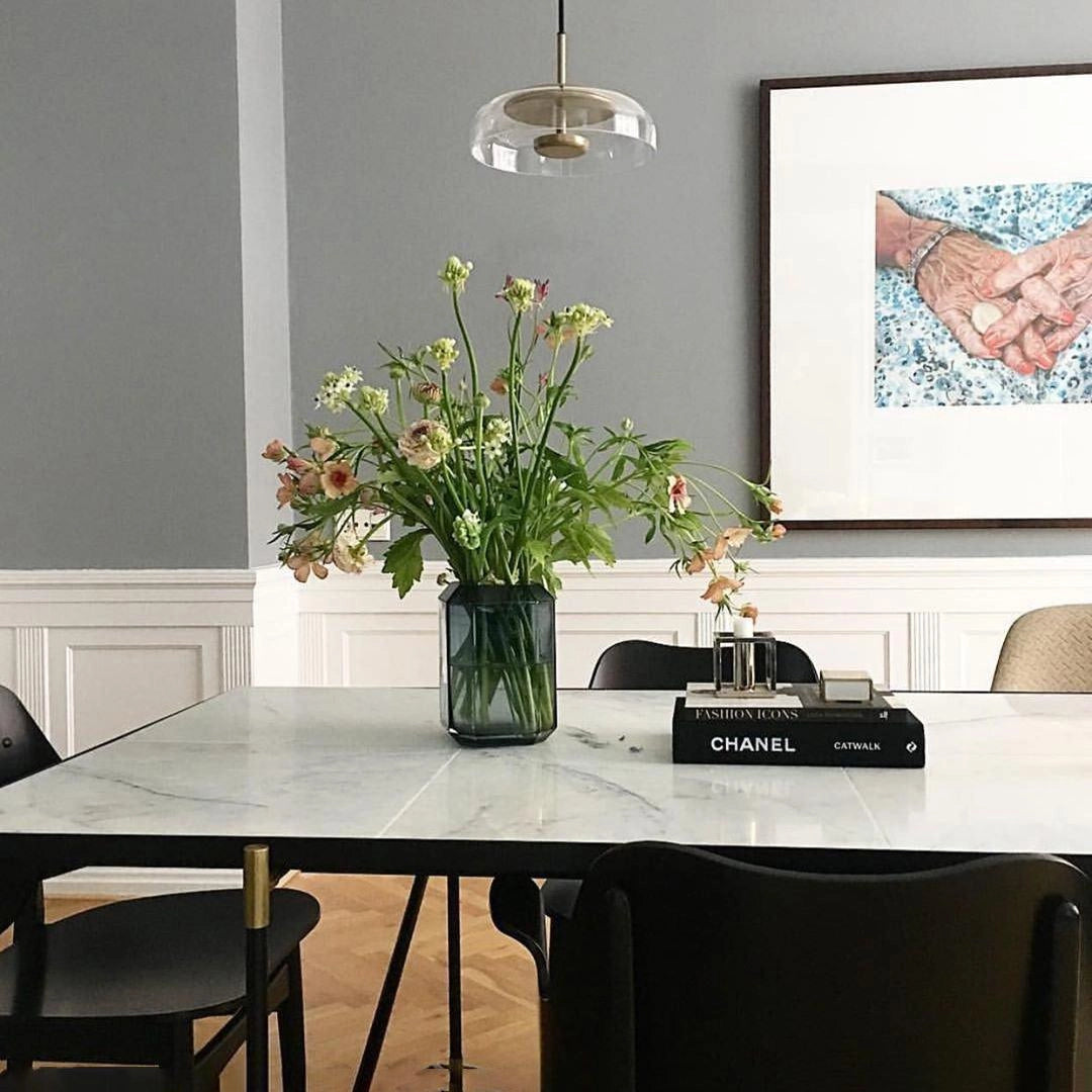Modern brass and chrome LED pendant lights hanging above a contemporary table with a vase of flowers and houseplants in a minimalist interior design setting.
