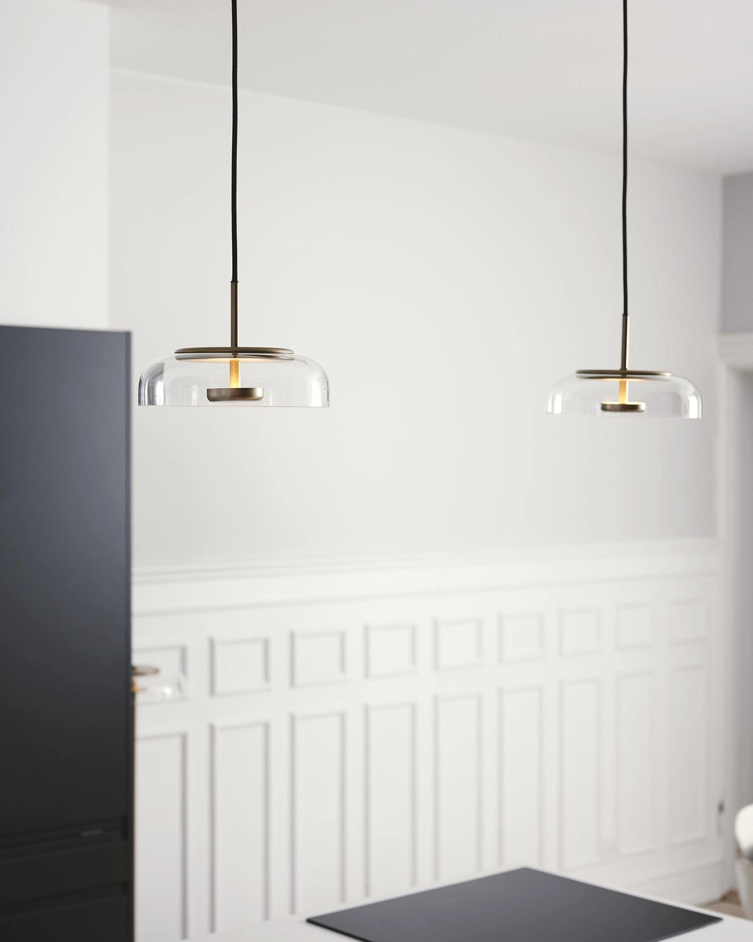 Modern brass and chrome LED pendant lights illuminating a minimalist room with wooden cabinetry and hardwood flooring.