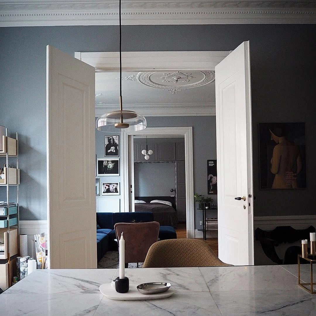 Modern brass and chrome LED pendant lights illuminating a minimalist living room with a grey couch and wooden table.