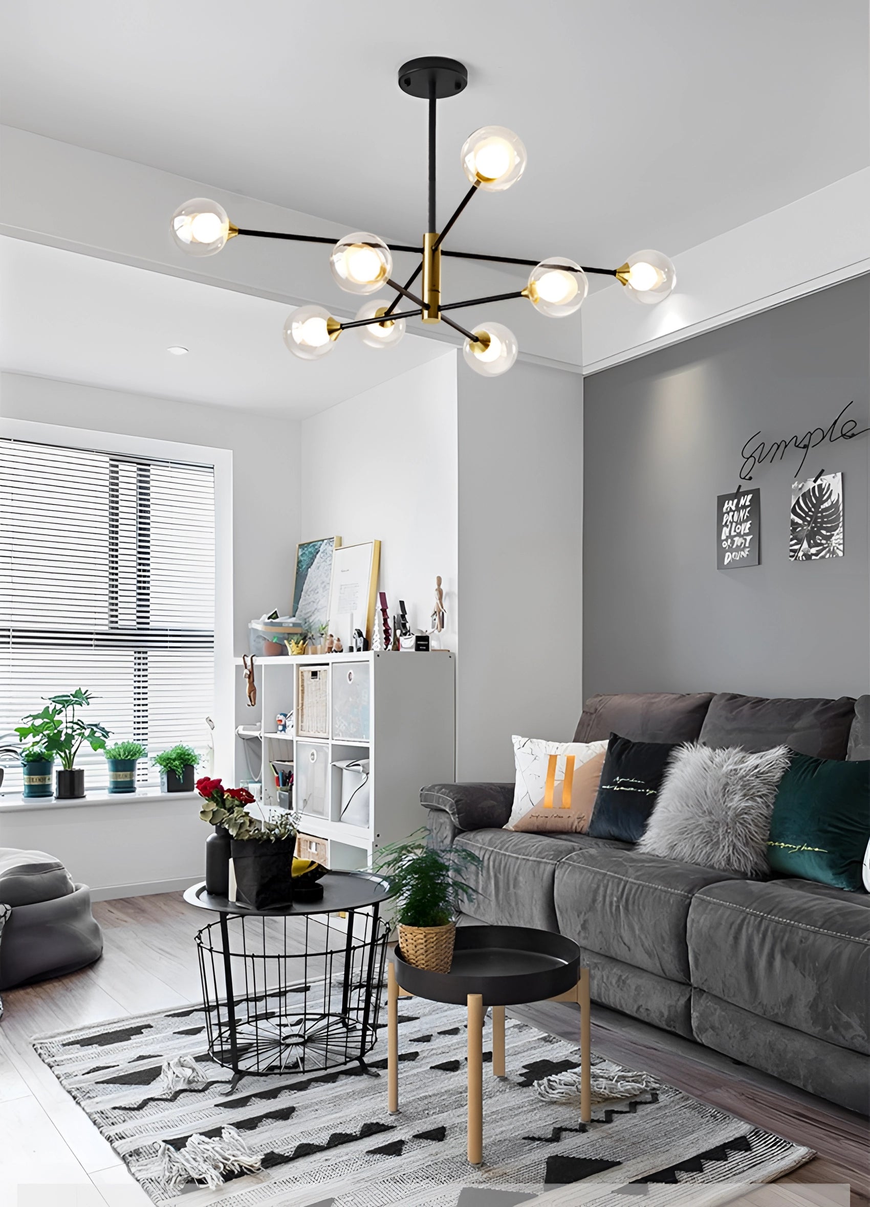 Modern living room featuring a grey couch, wooden table, and a geometric brass LED chandelier with mid-century minimalist design, complemented by houseplants and wood flooring.
