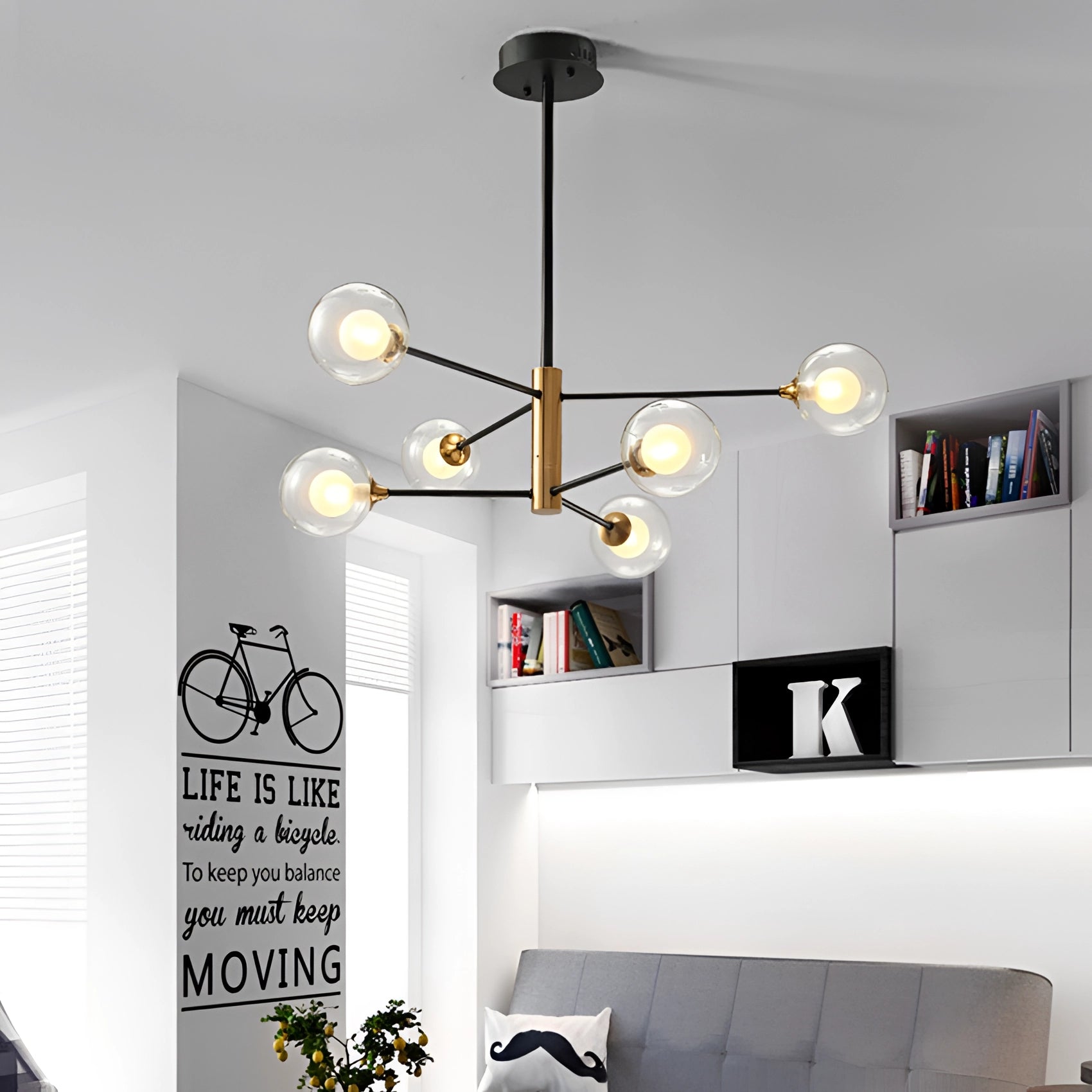 Modern brass geometric LED chandelier illuminating a minimalist mid-century interior with a couch and plant.