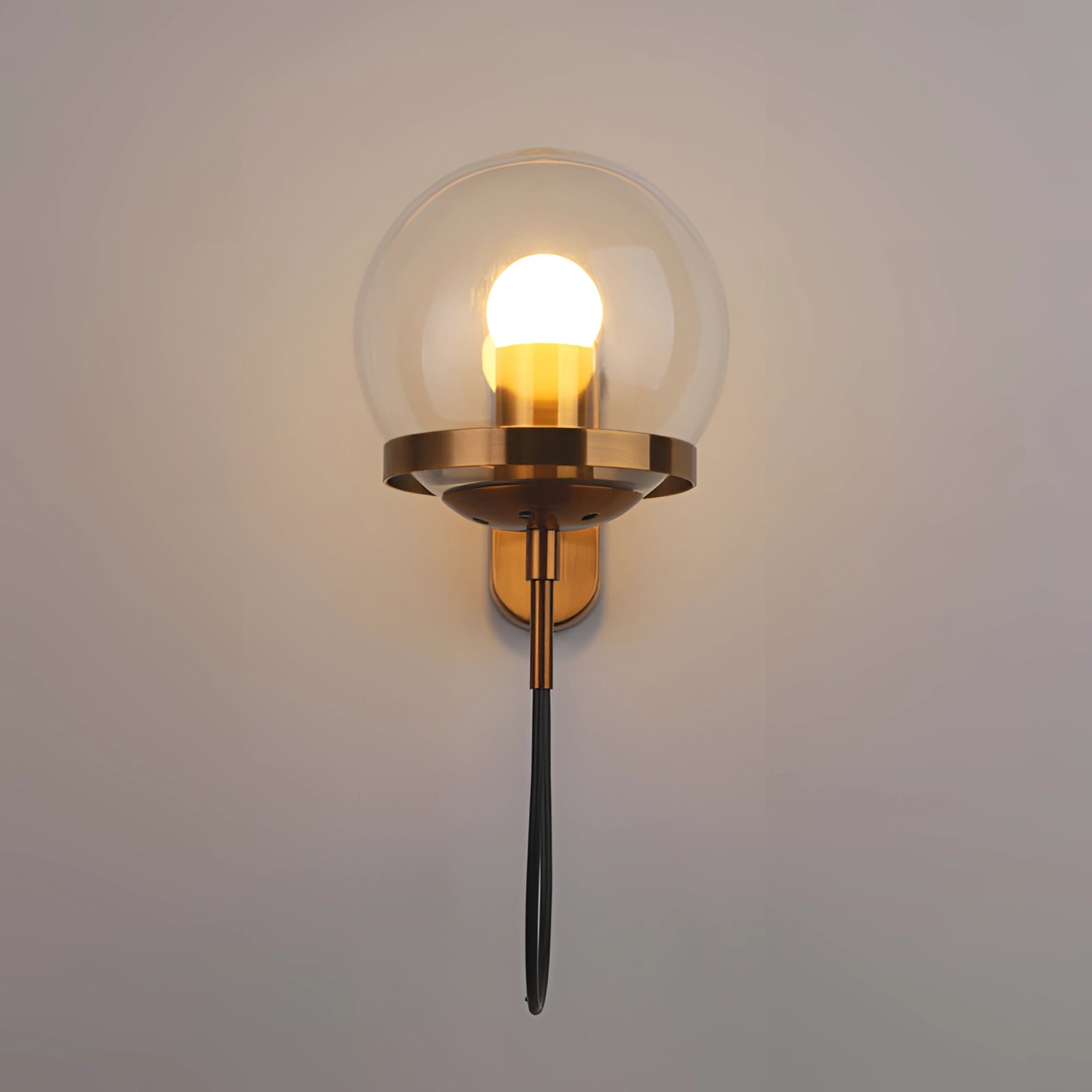 Modern brass globe wall sconce with a minimalist design, featuring a warm amber glow and mounted on a wooden base, illuminating a bedroom setting.