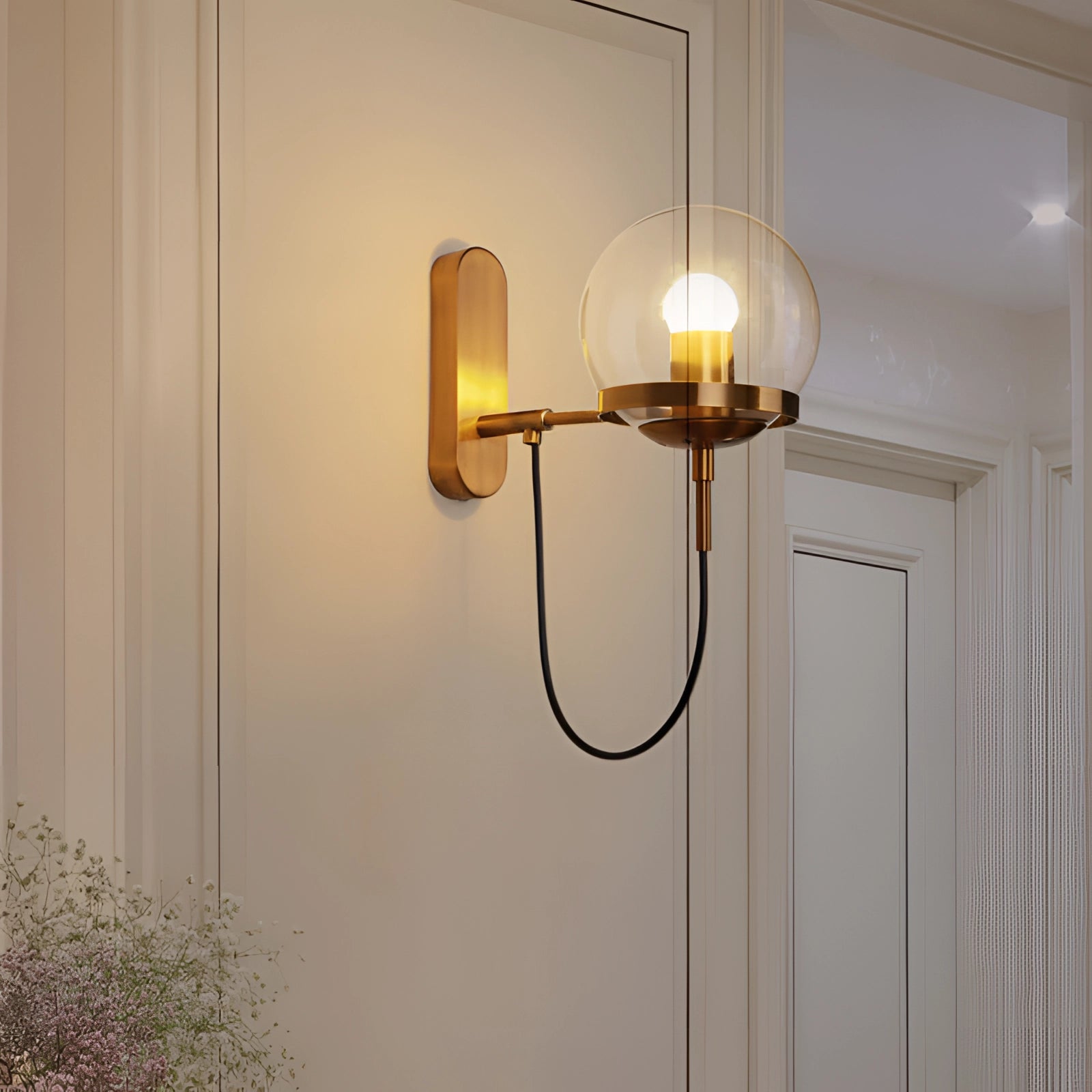 Modern brass globe wall sconce with a minimalist design, mounted on a wooden wall in a stylishly decorated interior featuring ambient lighting, a potted plant, and a warm amber glow.