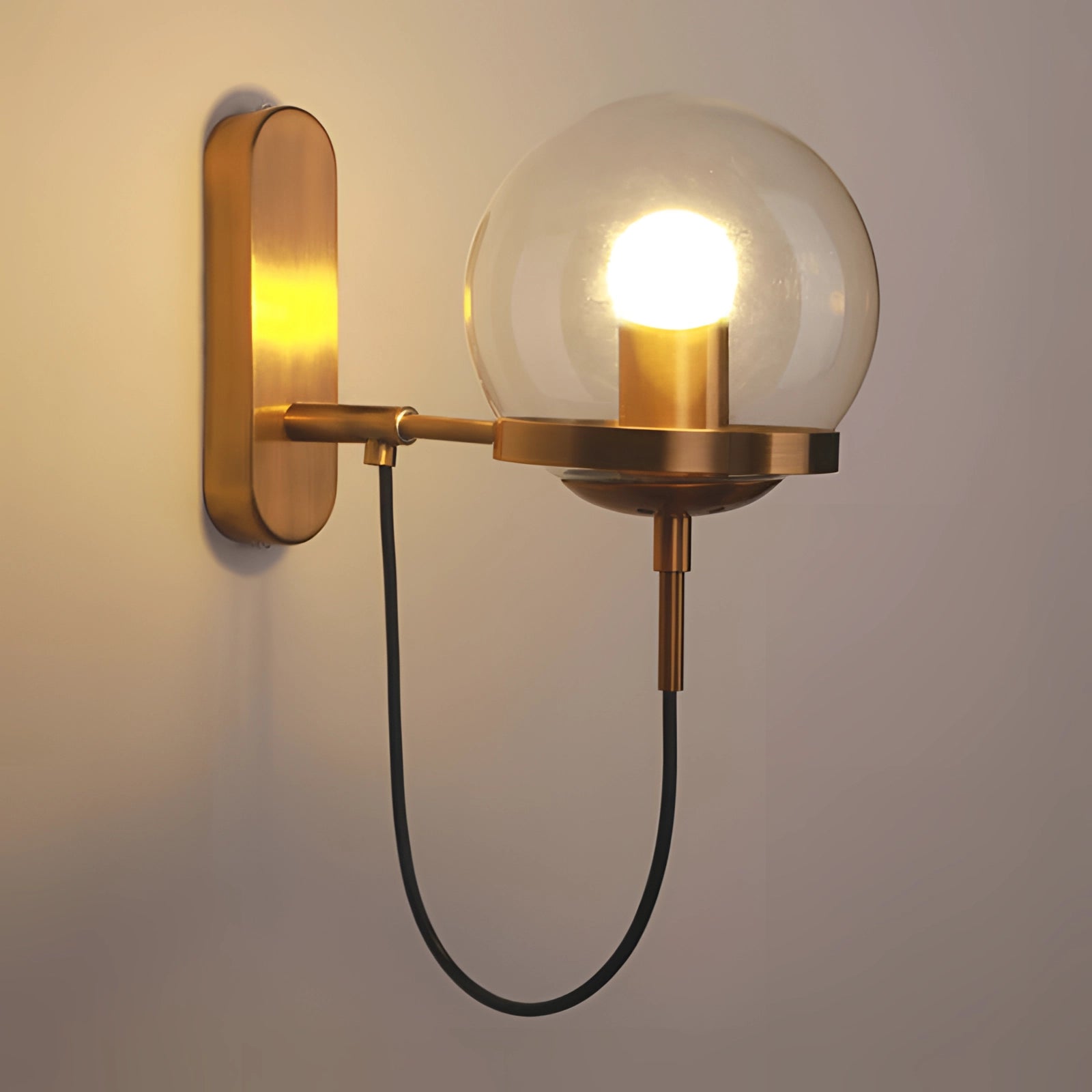 Modern brass globe wall sconce in bronze finish mounted on a wooden panel, emitting a warm amber light, ideal for minimalist bedroom décor.