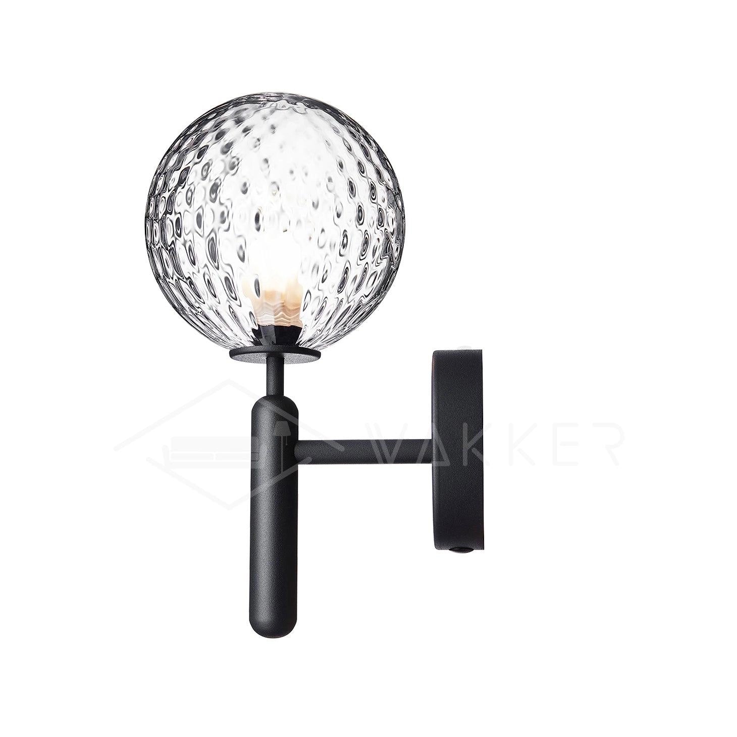 Modern brass globe wall sconce with LED light fixture, mounted beside a bed, featuring a sleek metal design and a circular lampshade.