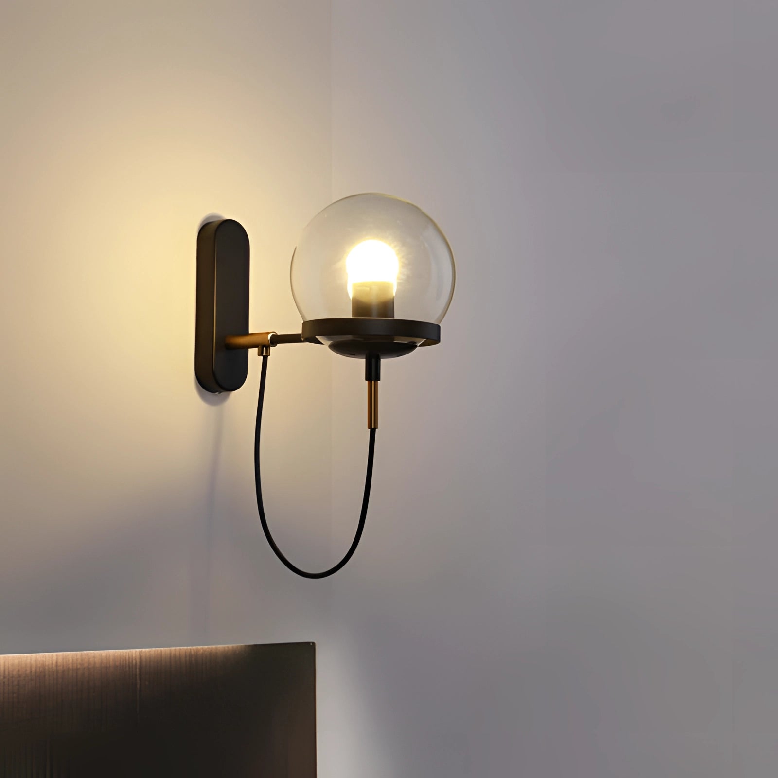 Modern brass globe wall sconce mounted on a wooden panel, featuring a minimalist design suitable for bedroom lighting. The fixture showcases a spherical metal lamp with a sleek finish.