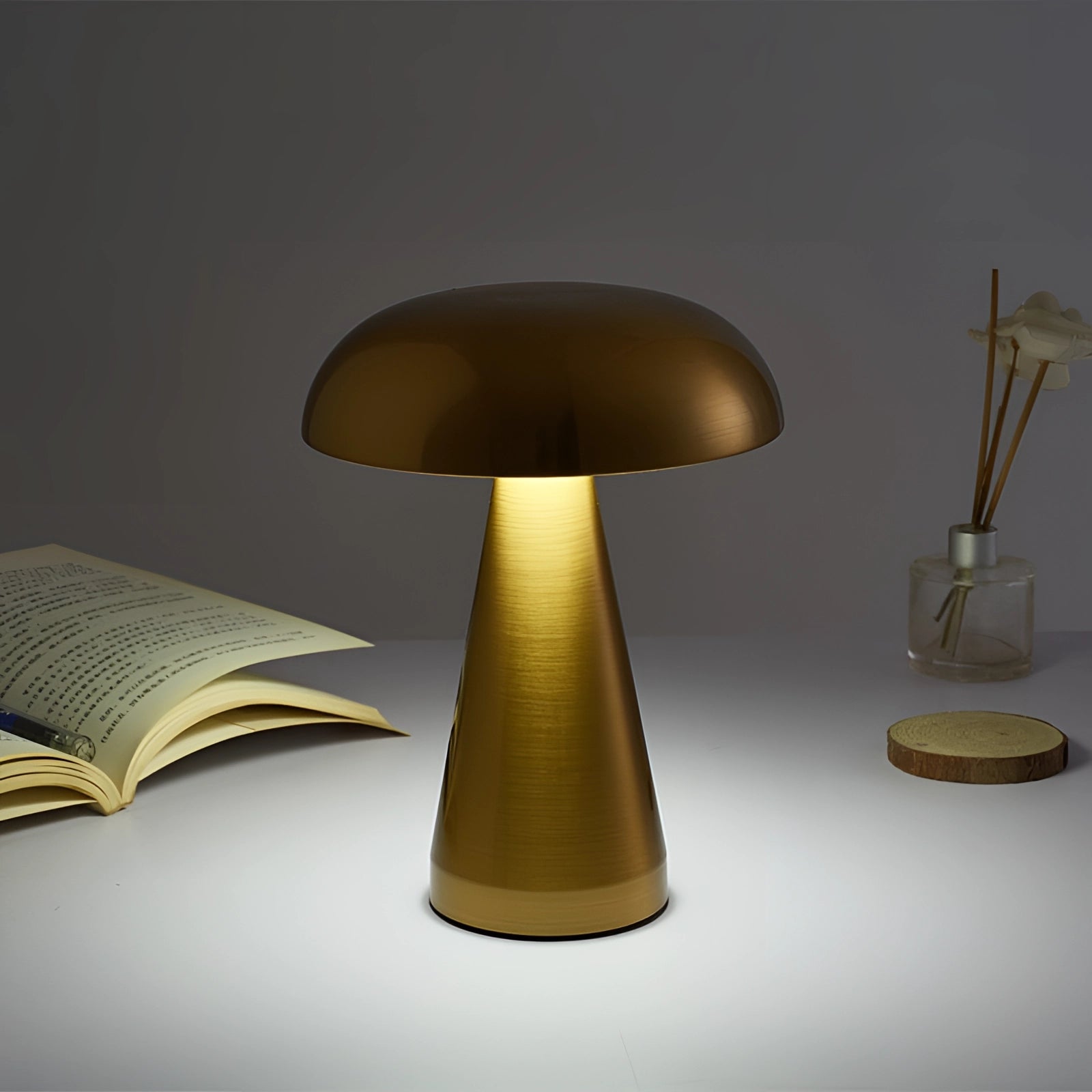 Modern brass mushroom lamp with a sleek minimalist design in gold, placed on a wooden table accompanied by books and art, emitting soft lighting with a stylish lampshade.