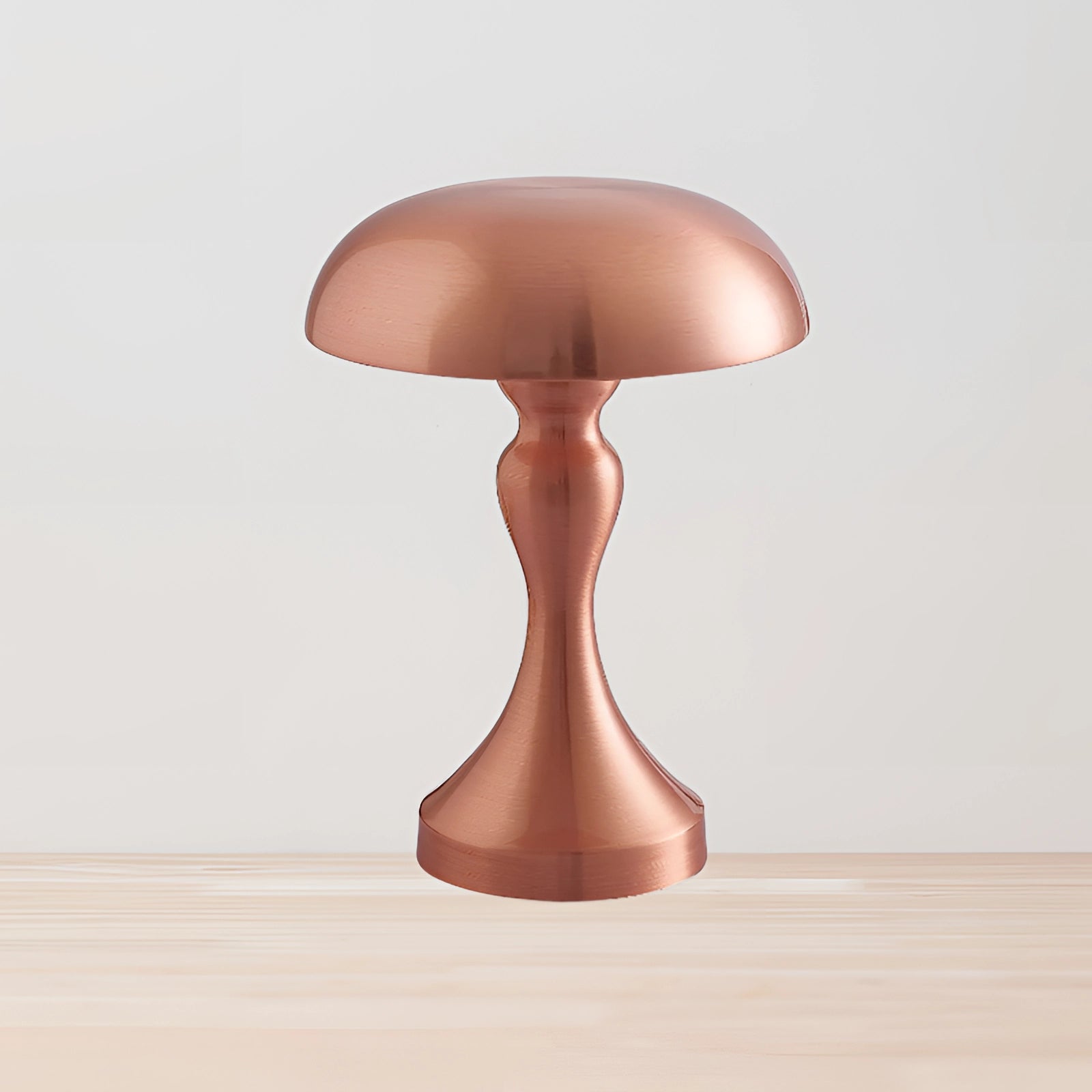 A rose gold modern brass mushroom table lamp with an elegant design, placed on a wooden surface, surrounded by plants.