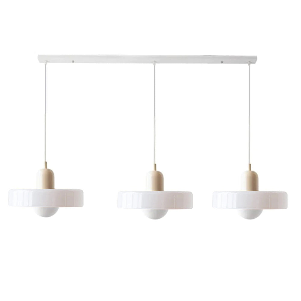 Modern brass pendant lights with adjustable red cables hanging from a ceiling, illuminating a kitchen with wooden shelves and table.