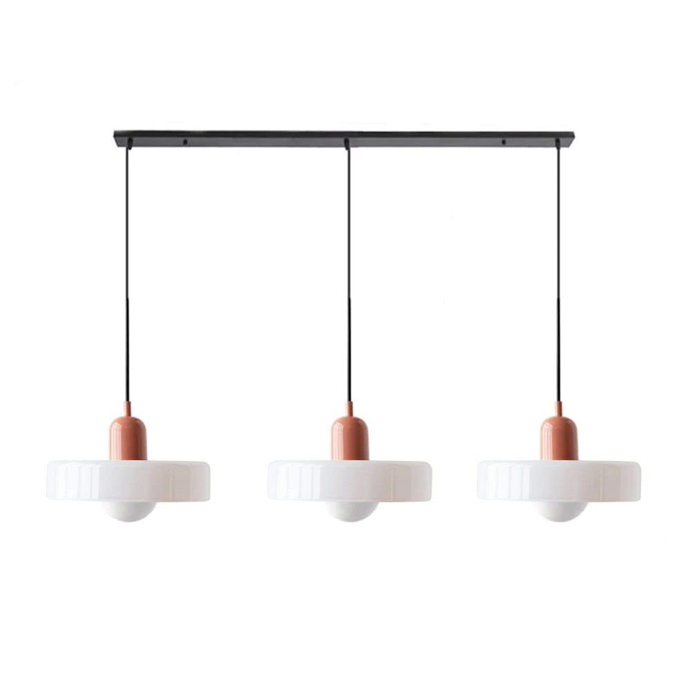 Modern brass pendant light with a red cable hanging from the ceiling above a wooden table, complemented by indoor plants and industrial kitchen decor.