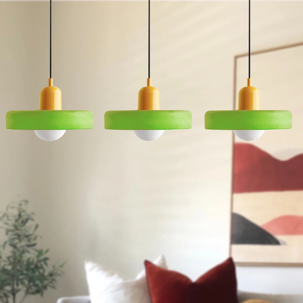 Modern brass pendant lights with three matte green and yellow heads, adjustable red cable, hanging in an industrial kitchen setting with white walls and wooden accents.