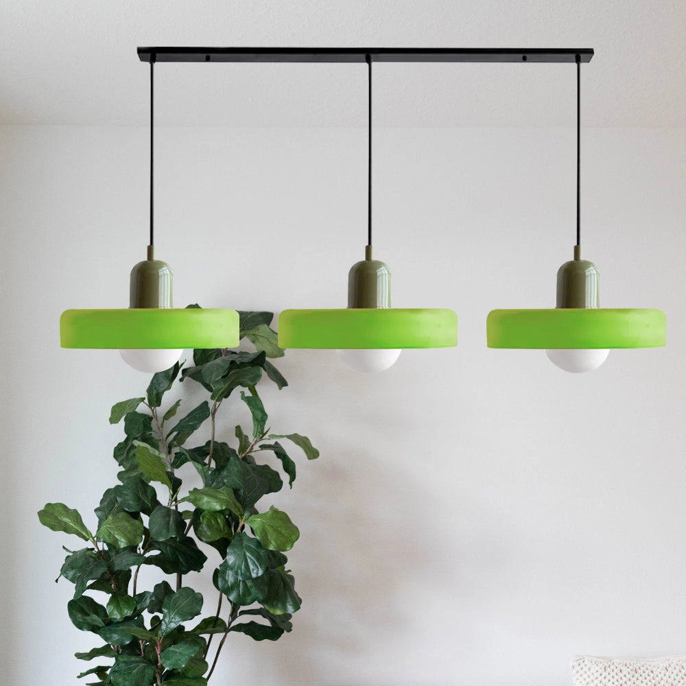 Modern brass pendant lights with adjustable height and red cable, hanging in an industrial kitchen setting, with surrounding wooden shelves, plants, and herbs.