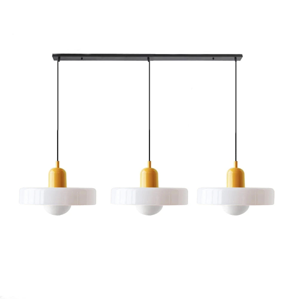 Modern brass pendant light with adjustable height and red cable, hanging from the ceiling over a kitchen table with metal accents and shelves in the background.